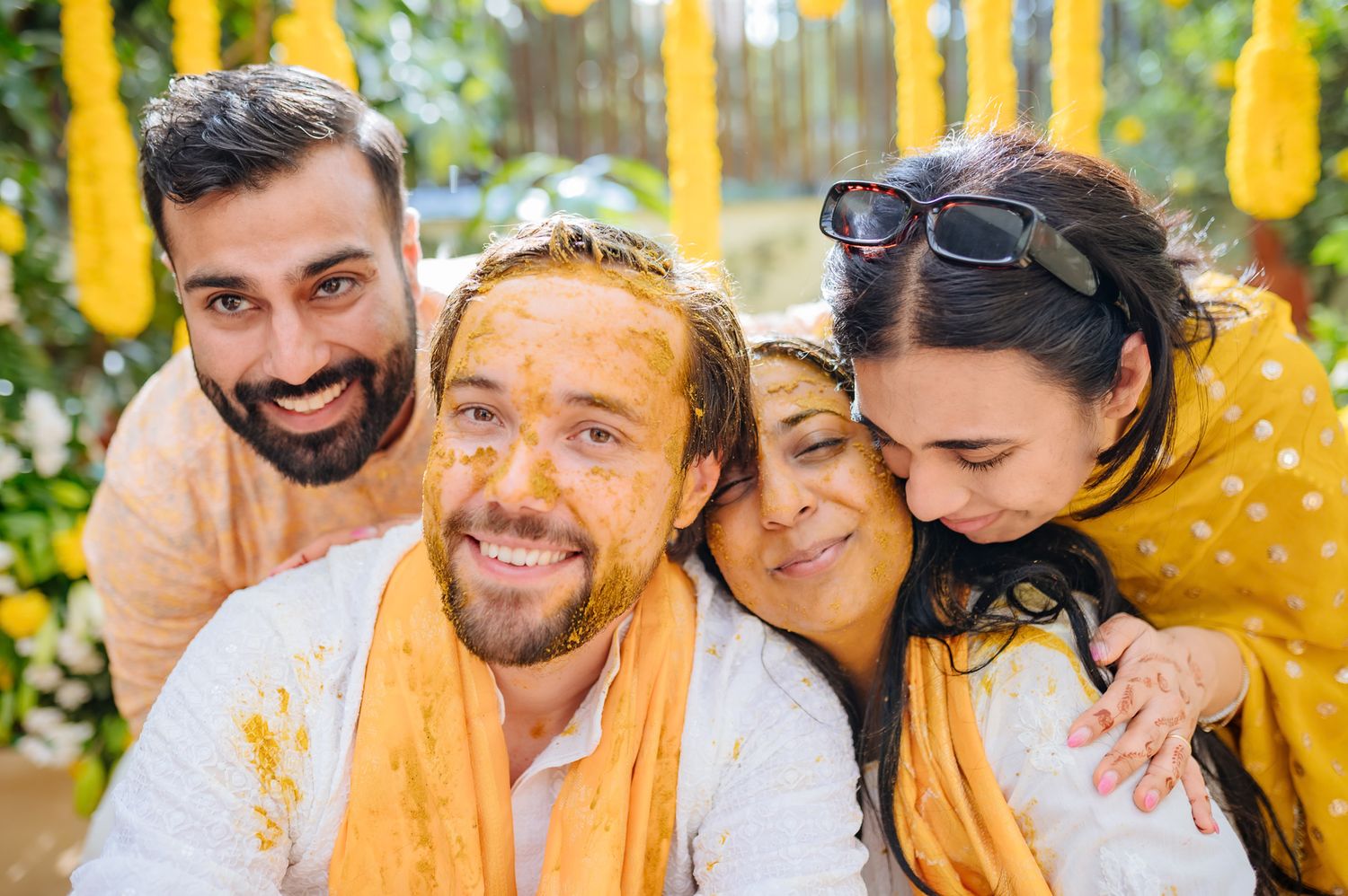 Bride and groom covered in turmeric during an Indo-Norwegian wedding and Family applying Haldi to the bride during a joyful wedding ritual