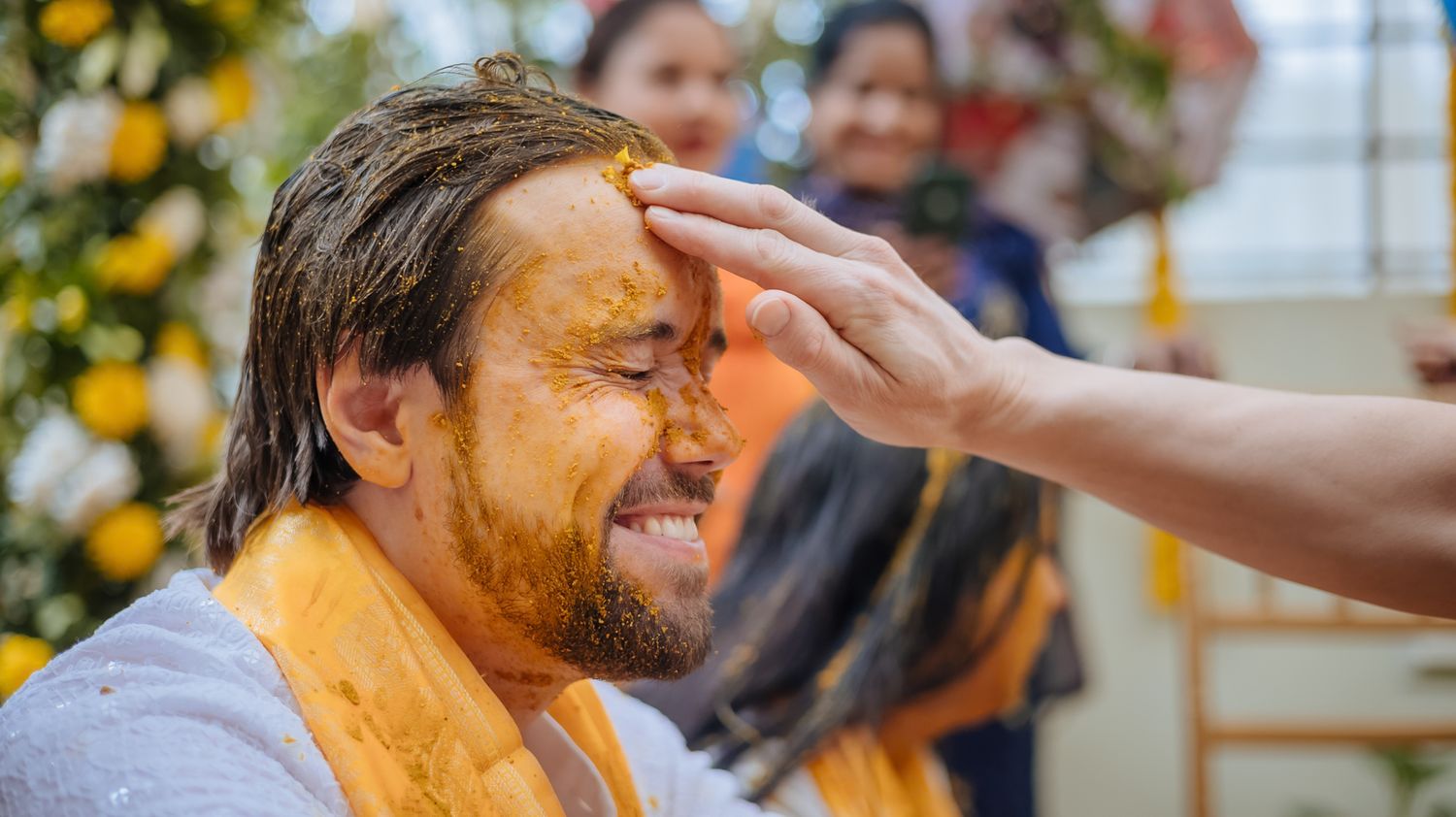 Bride and groom covered in turmeric during an Indo-Norwegian wedding and Family applying Haldi to the bride during a joyful wedding ritual