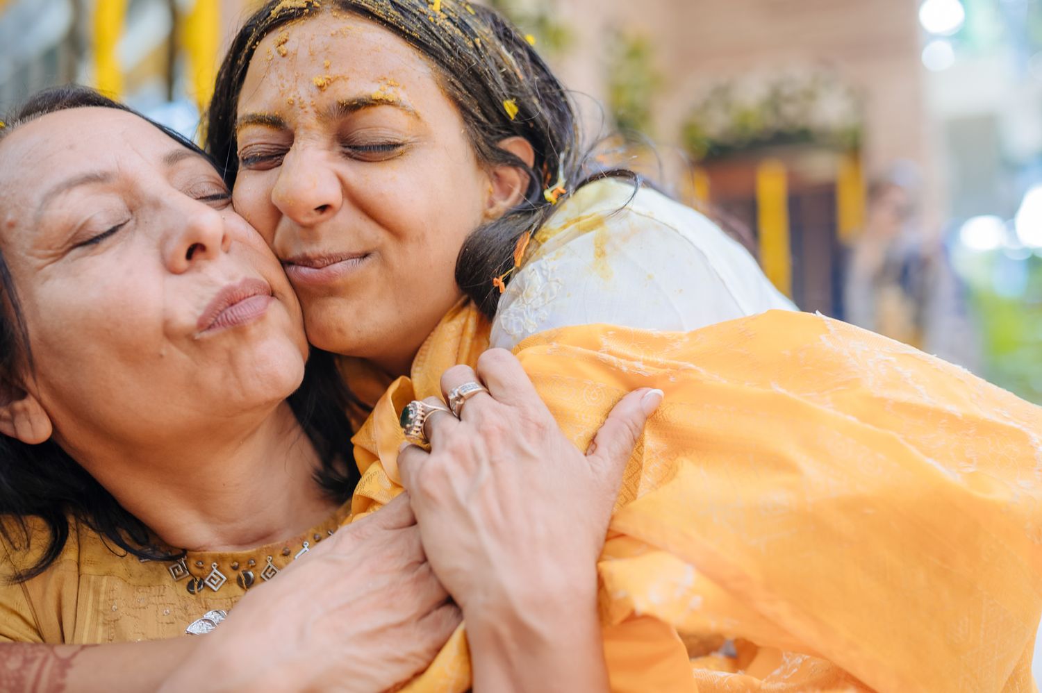 Bride and groom covered in turmeric during an Indo-Norwegian wedding and Family applying Haldi to the bride during a joyful wedding ritual