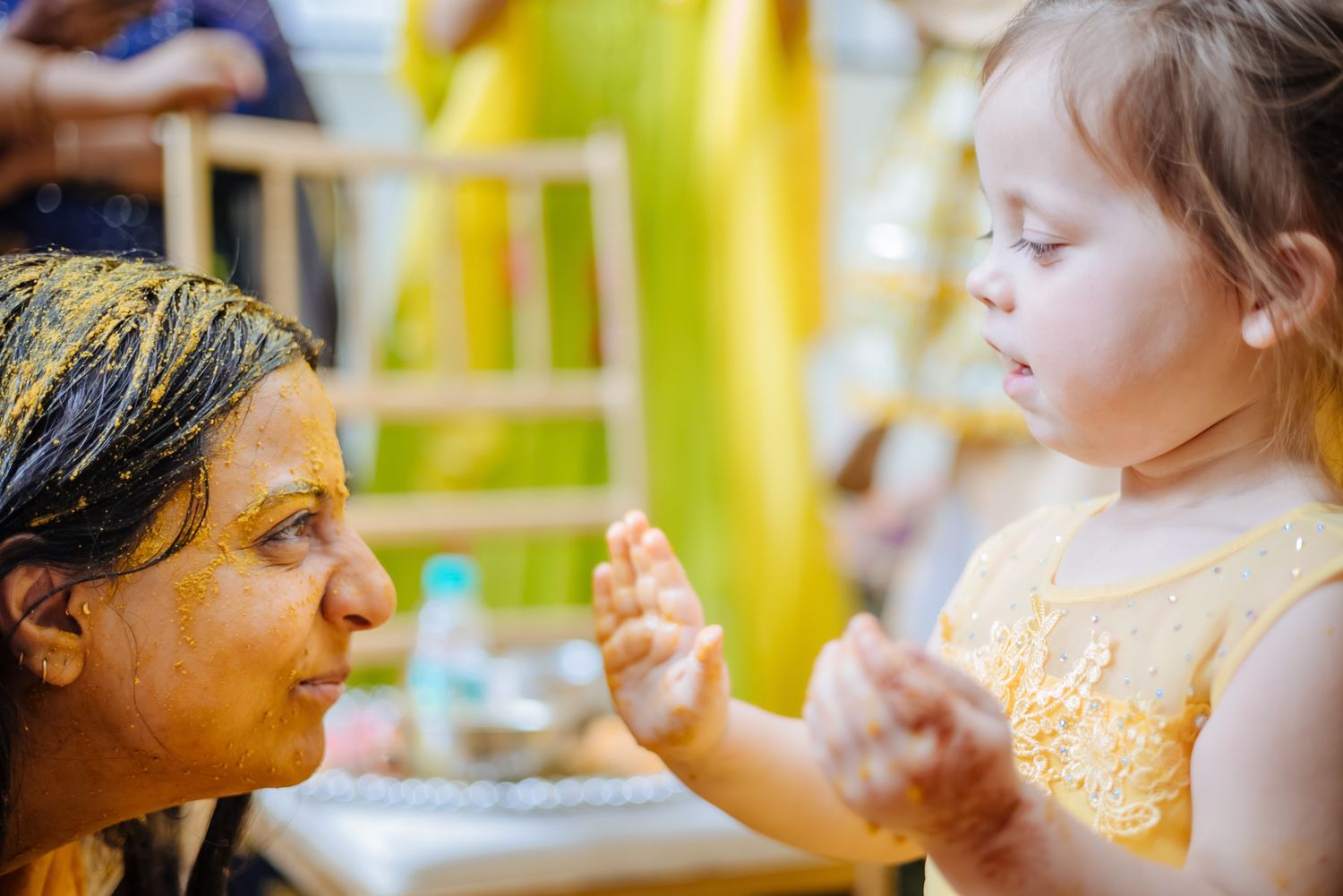 Bride and groom covered in turmeric during an Indo-Norwegian wedding and Family applying Haldi to the bride during a joyful wedding ritual