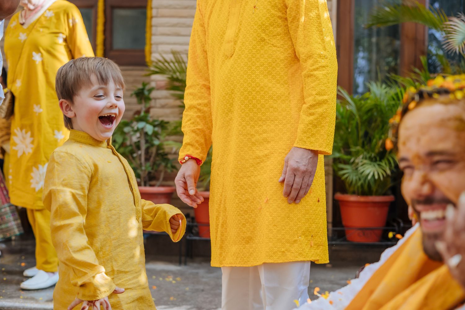 Bride and groom covered in turmeric during an Indo-Norwegian wedding and Family applying Haldi to the bride during a joyful wedding ritual