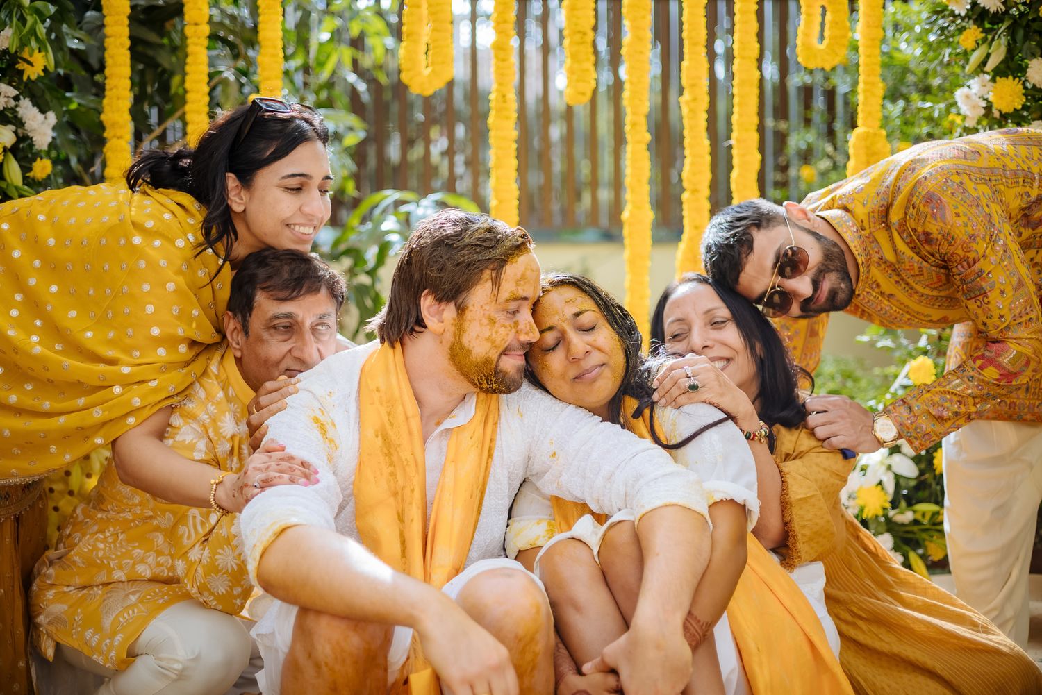 Bride and groom covered in turmeric during an Indo-Norwegian wedding and Family applying Haldi to the bride during a joyful wedding ritual