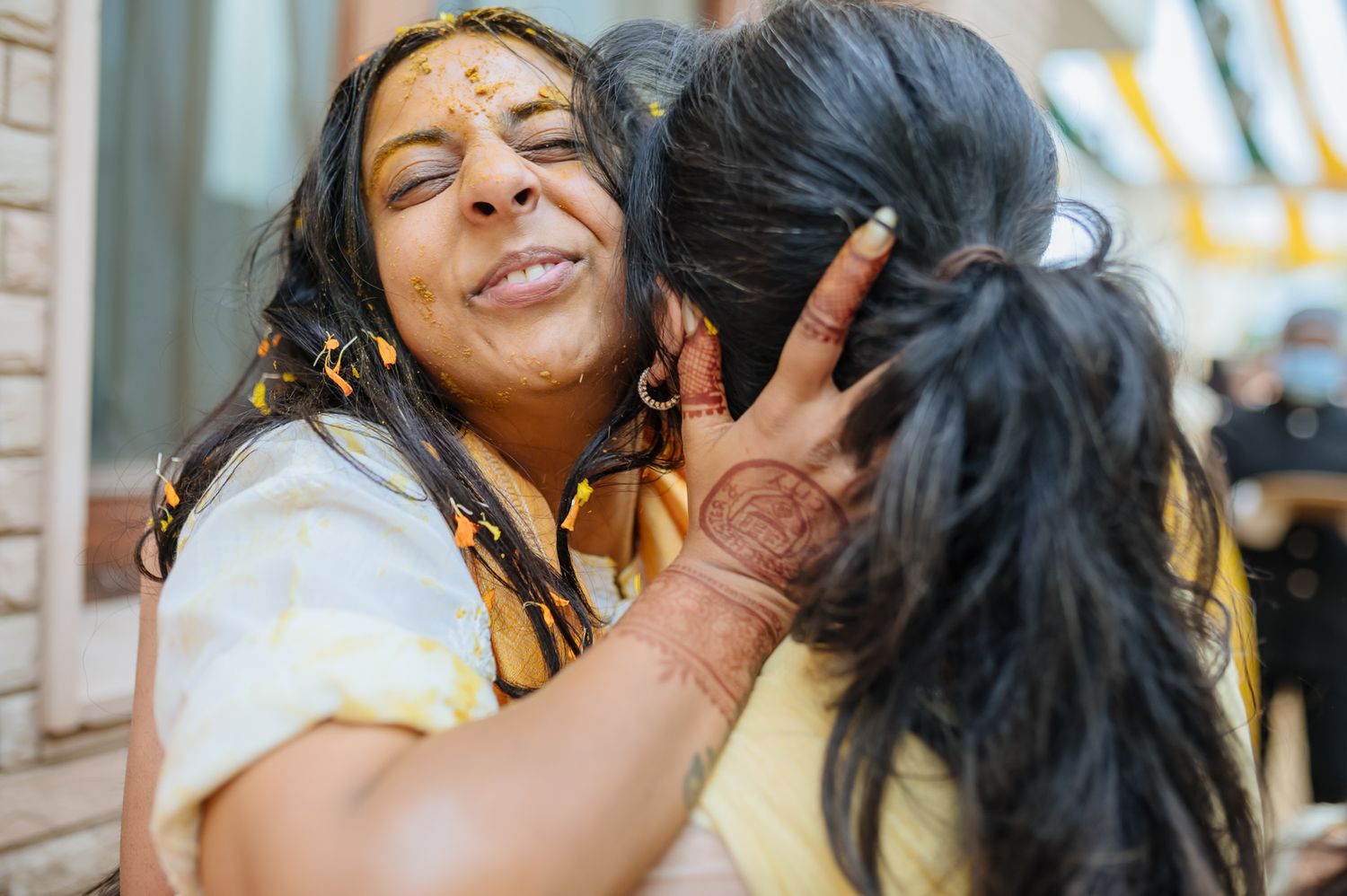 Bride and groom covered in turmeric during an Indo-Norwegian wedding and Family applying Haldi to the bride during a joyful wedding ritual