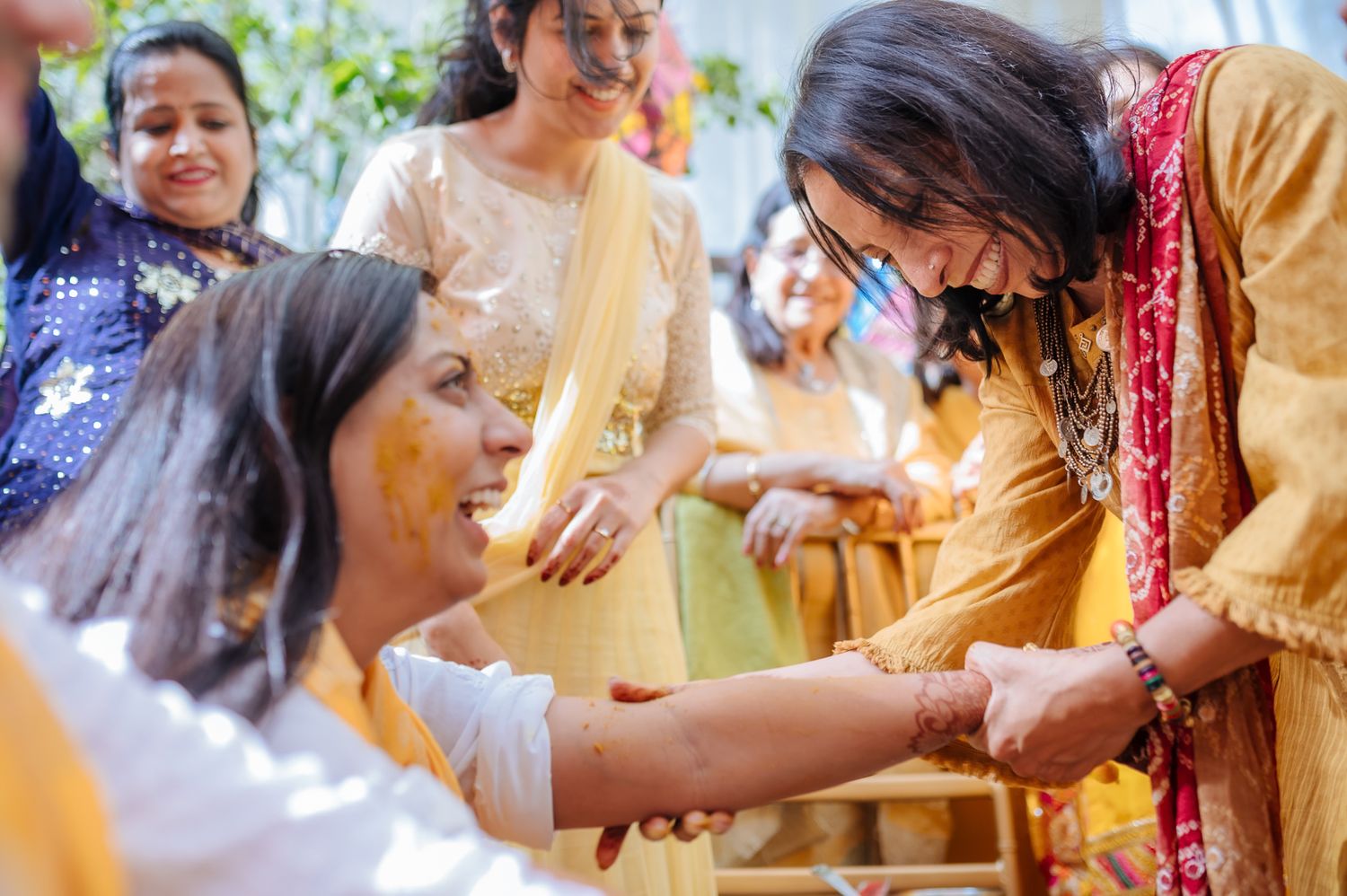 Bride and groom covered in turmeric during an Indo-Norwegian wedding and Family applying Haldi to the bride during a joyful wedding ritual
