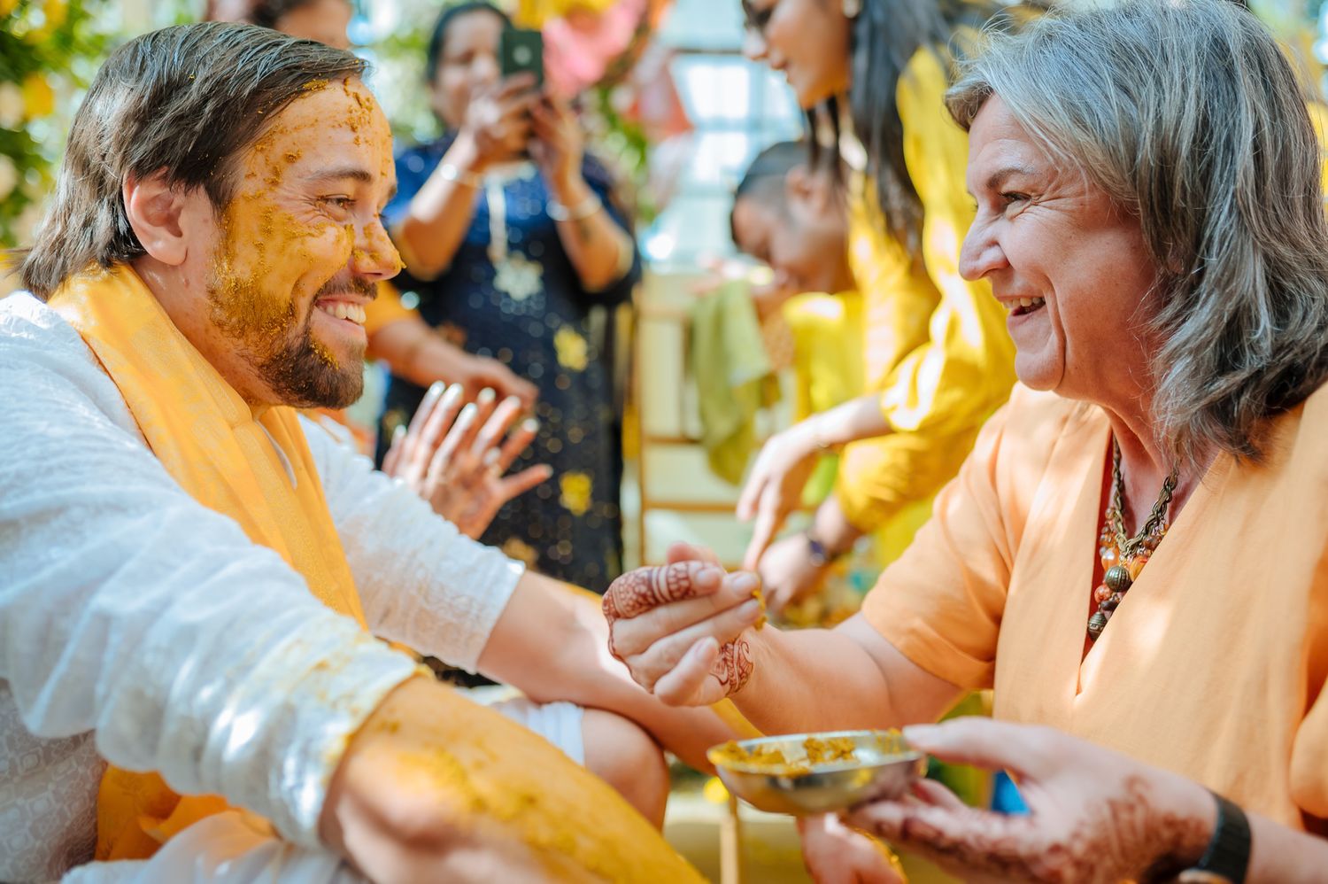 Bride and groom covered in turmeric during an Indo-Norwegian wedding and Family applying Haldi to the bride during a joyful wedding ritual