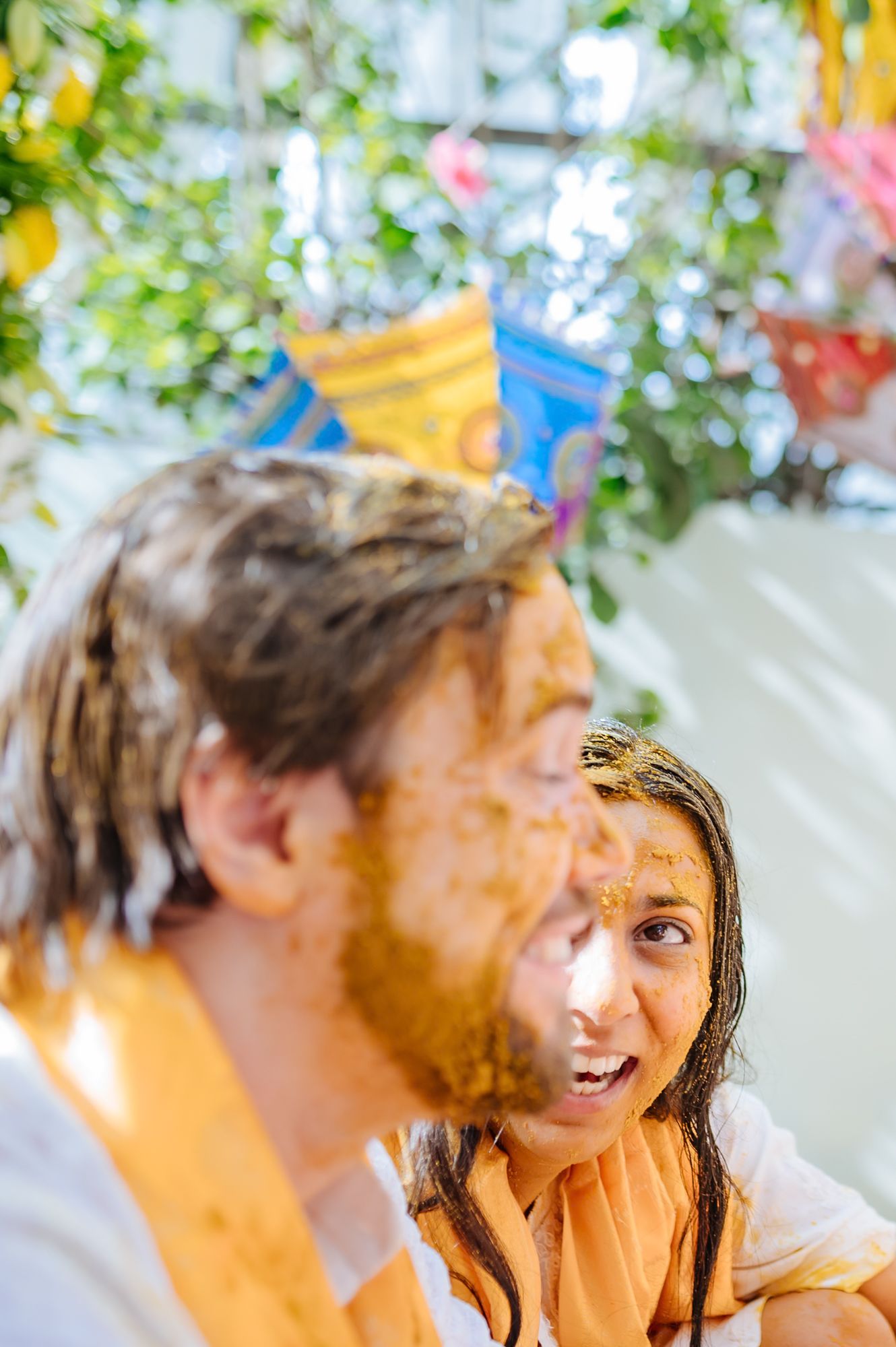 Bride and groom covered in turmeric during an Indo-Norwegian wedding and Family applying Haldi to the bride during a joyful wedding ritual