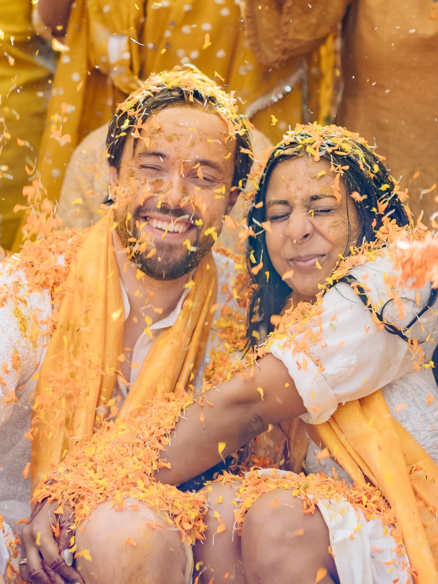 Bride and groom covered in turmeric during an Indo-Norwegian wedding and Family applying Haldi to the bride during a joyful wedding ritual