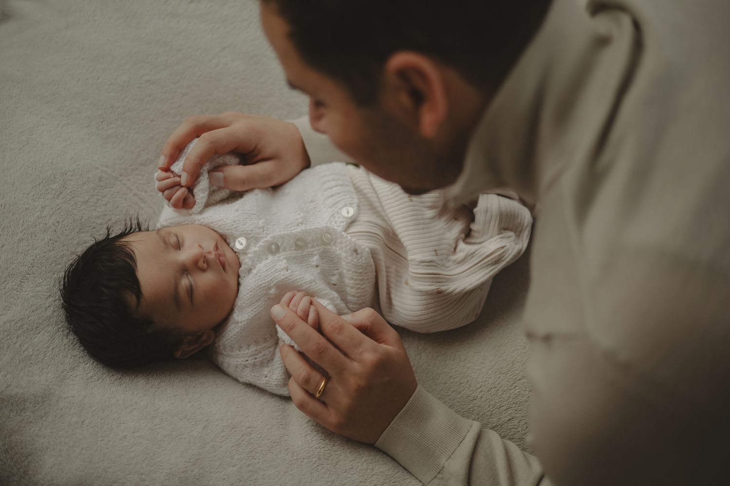 Baby holding dads hands during newborn shoot.
