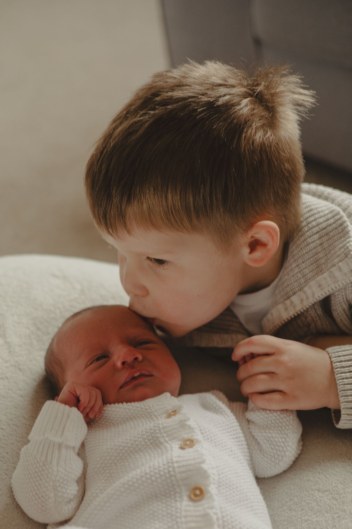 Brother kissing baby sister on head during newborn photography shoot.