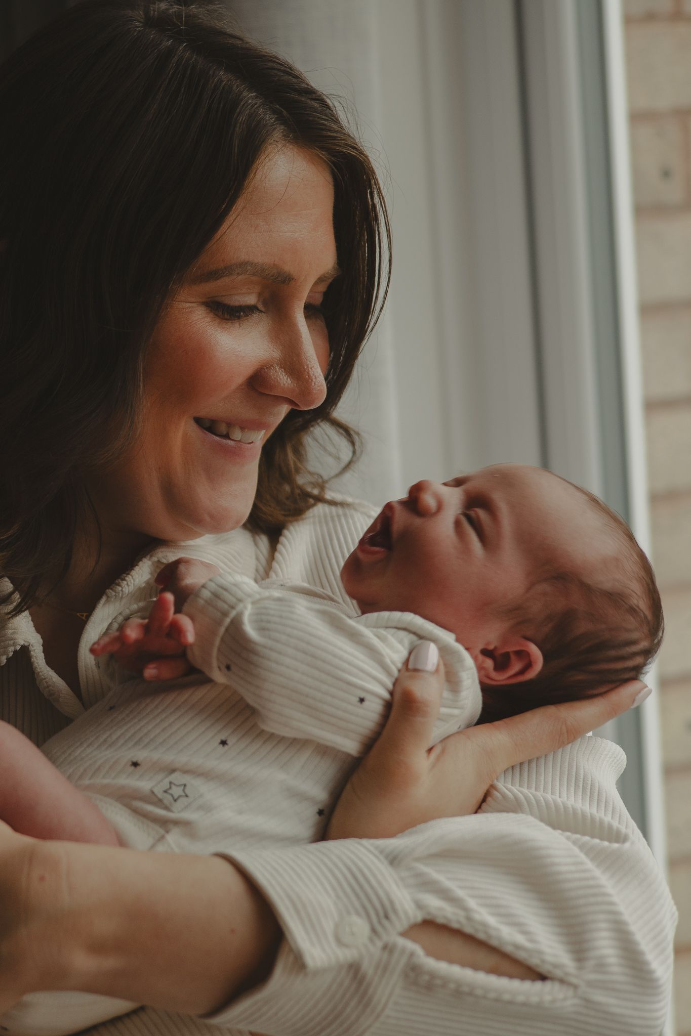 A newborn baby in their mothers arms smiling down.