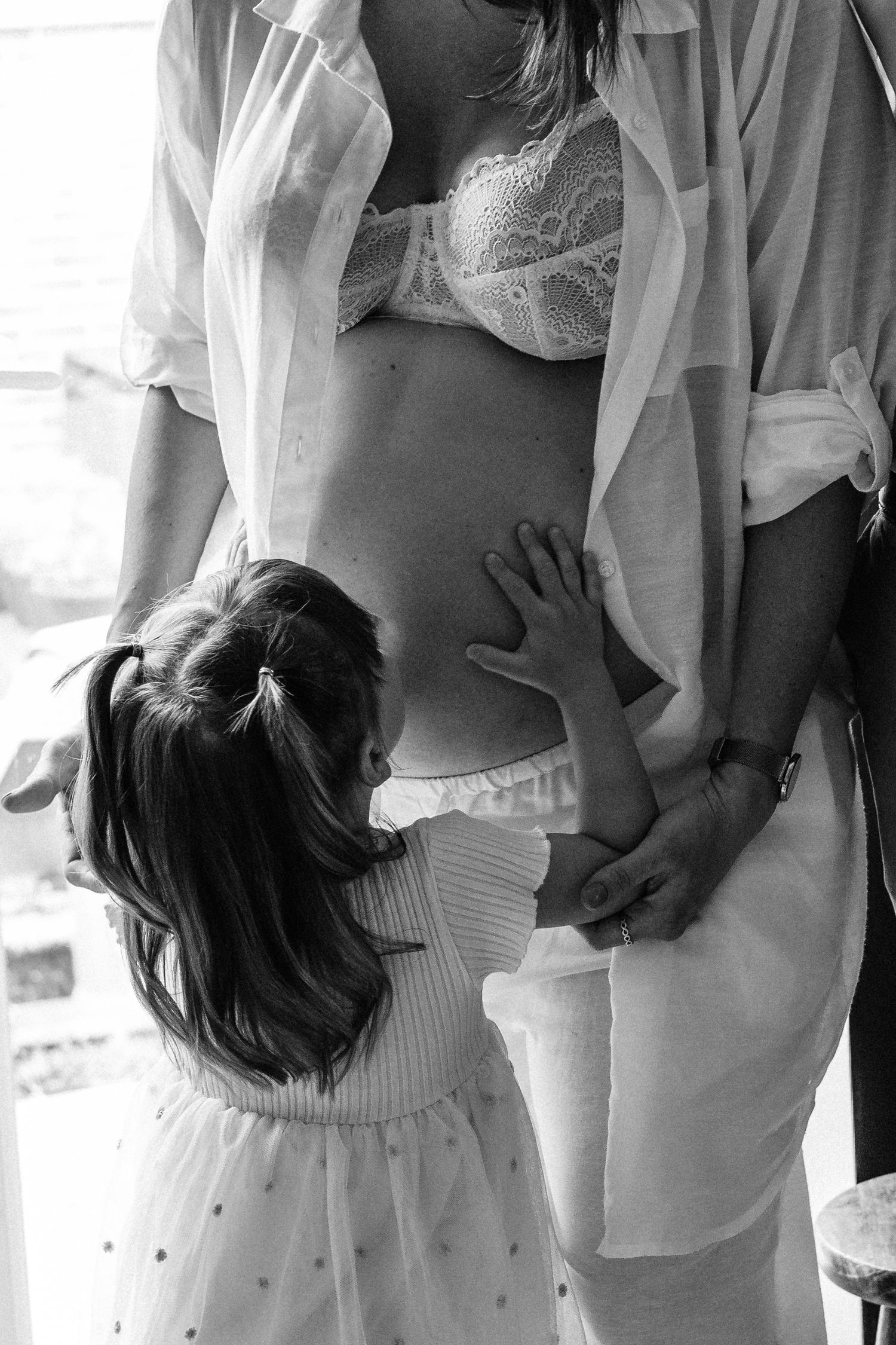 Big sister kissing baby bump on mum during maternity photoshoot.