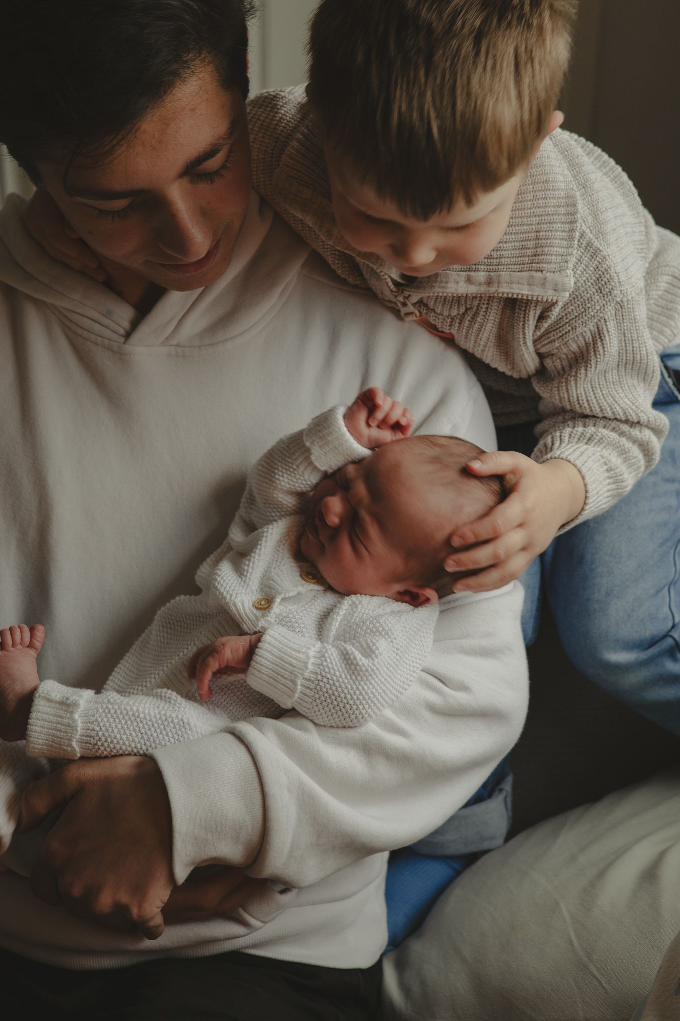 A newborn baby asleep in brothers arms with brothers looking down during a newborn shoot in Telford, Shropshire.
