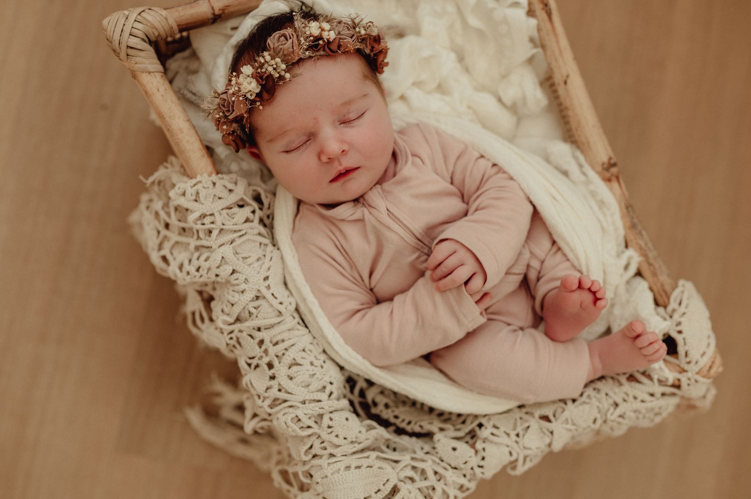 Sleeping newborn baby in pink outfit lying on delicate lace backdrop.