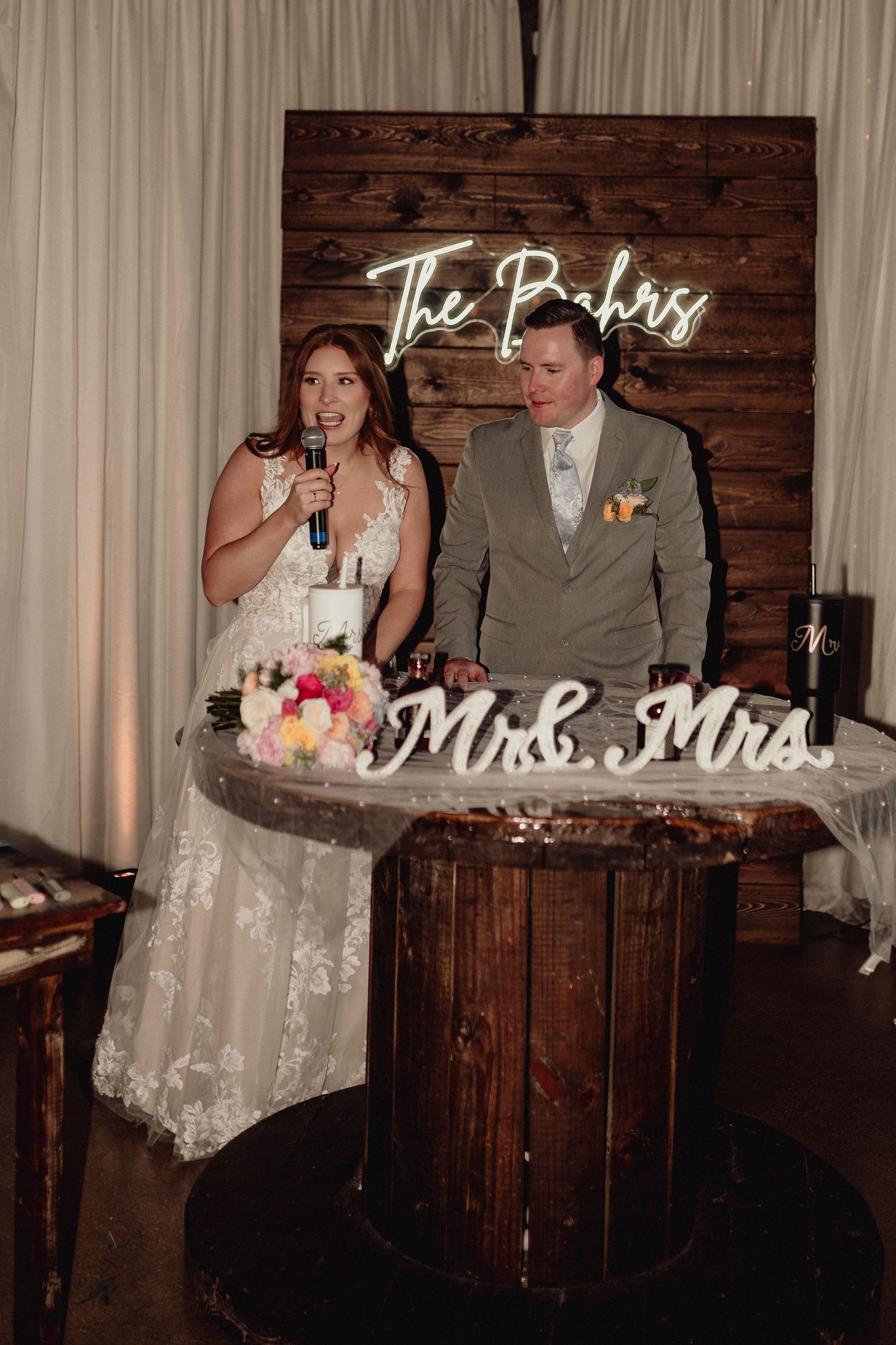 Wedding reception scene with rustic wooden bar and illuminated Mr & Mrs sign.
