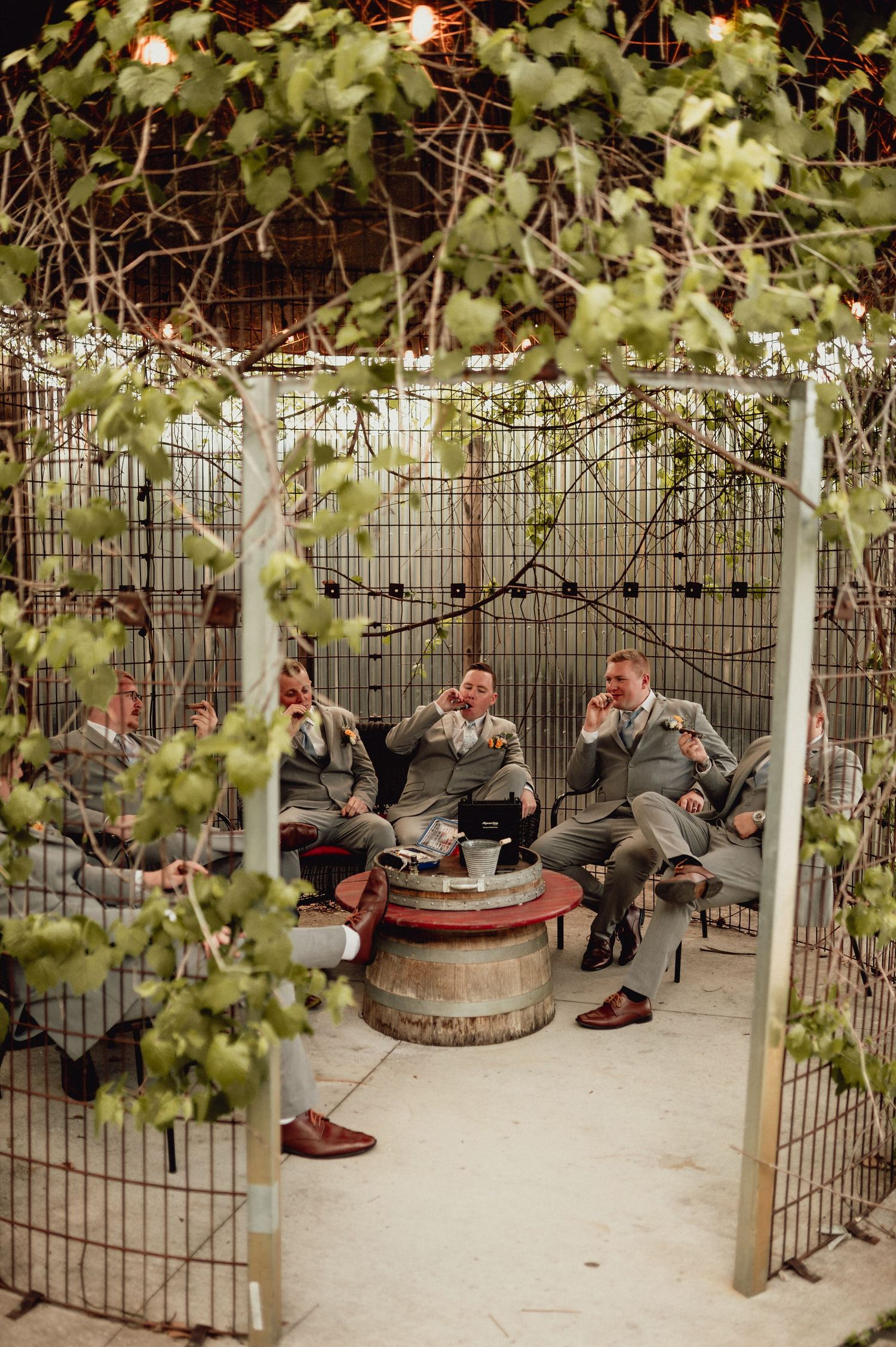 People relax under a vine-covered pergola in an outdoor garden seating area.