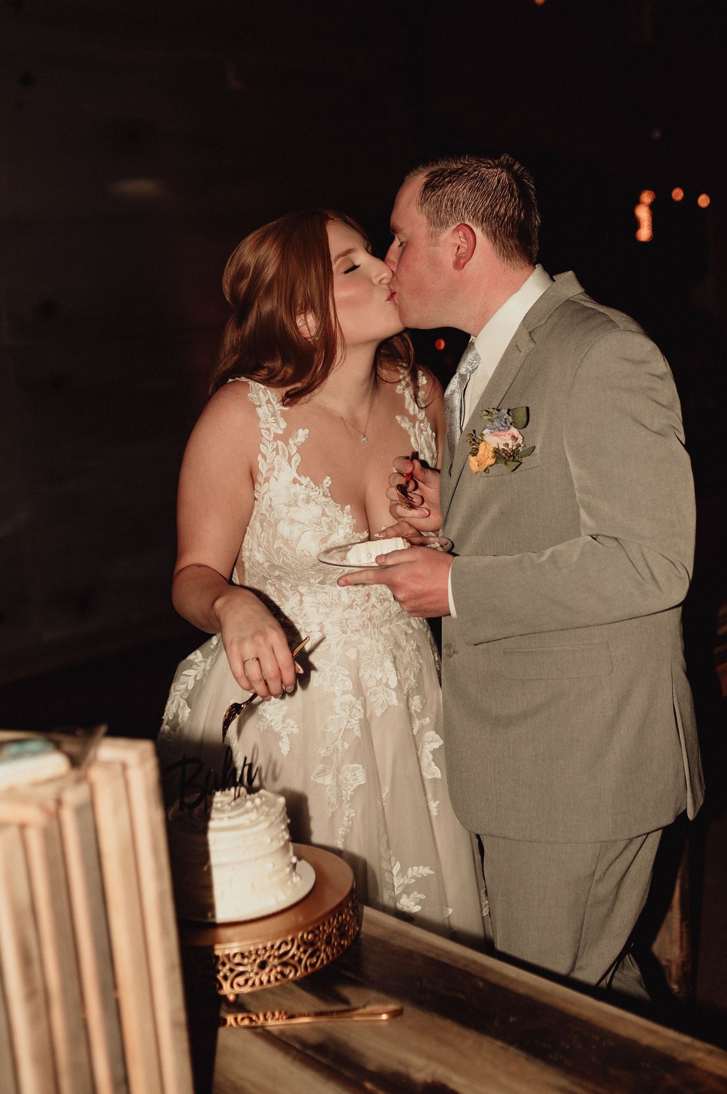 A couple in wedding attire shares a romantic kiss while seated at their reception table.