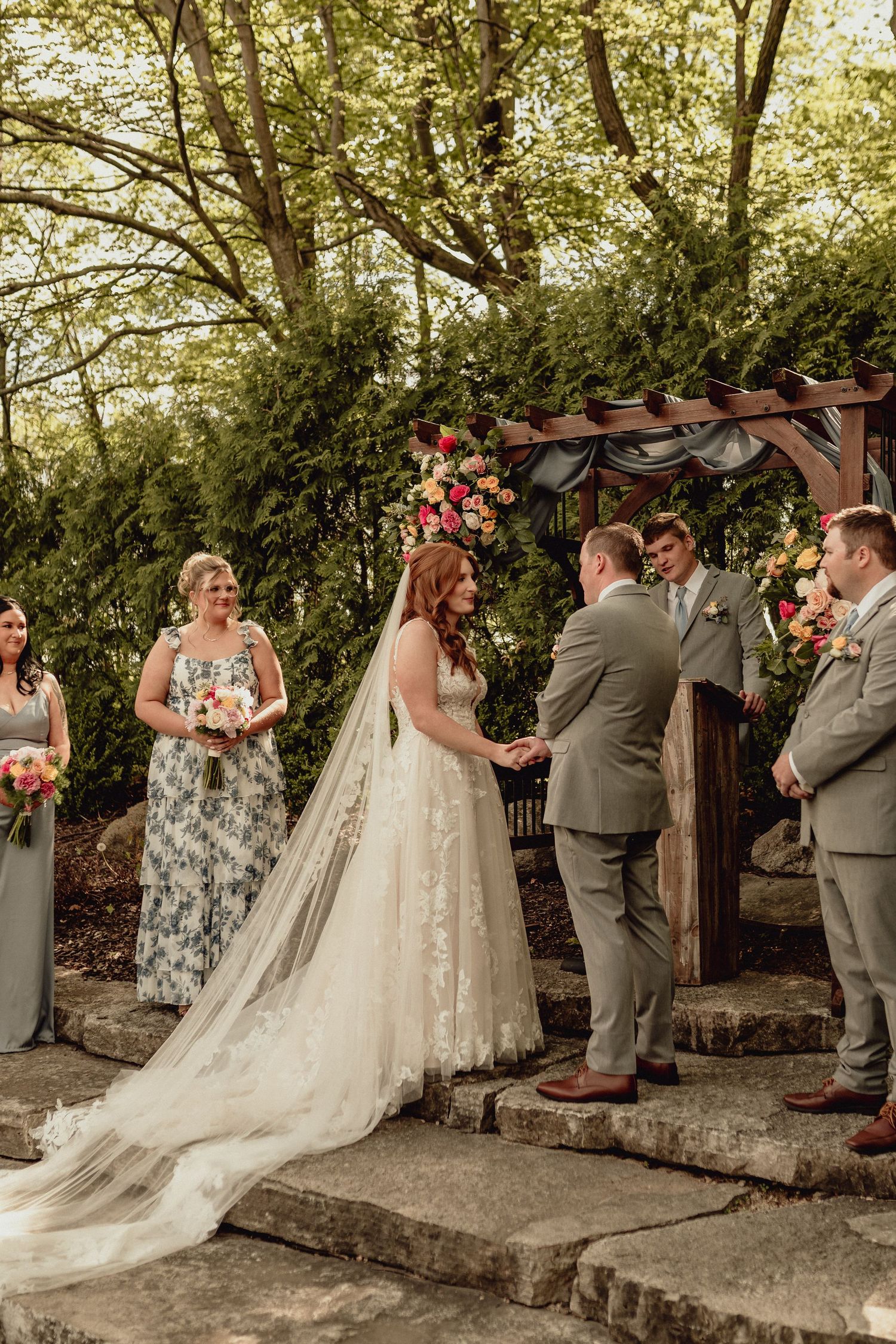 Wedding party stands in line against natural stone wall backdrop during outdoor forest ceremony.