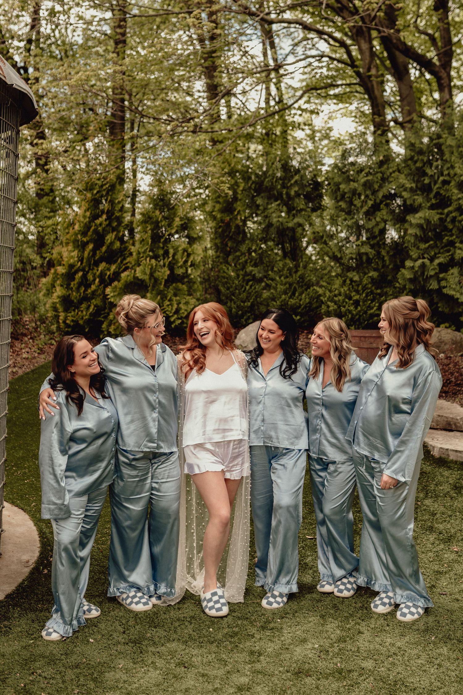 A group in matching blue satin pajamas laughing together on grass during an outdoor gathering.