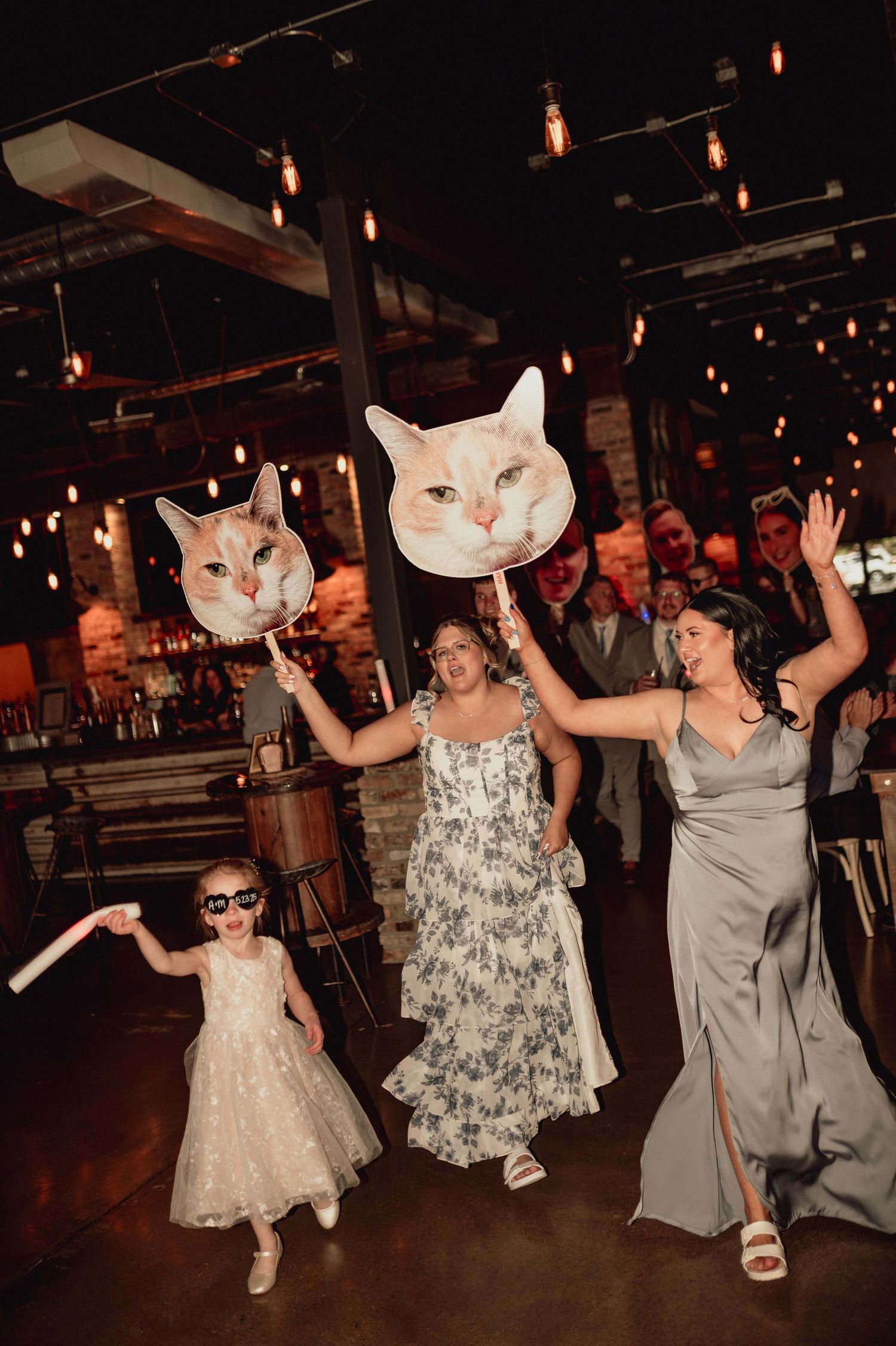 People dancing and celebrating at a dimly lit indoor venue with hanging lights overhead.