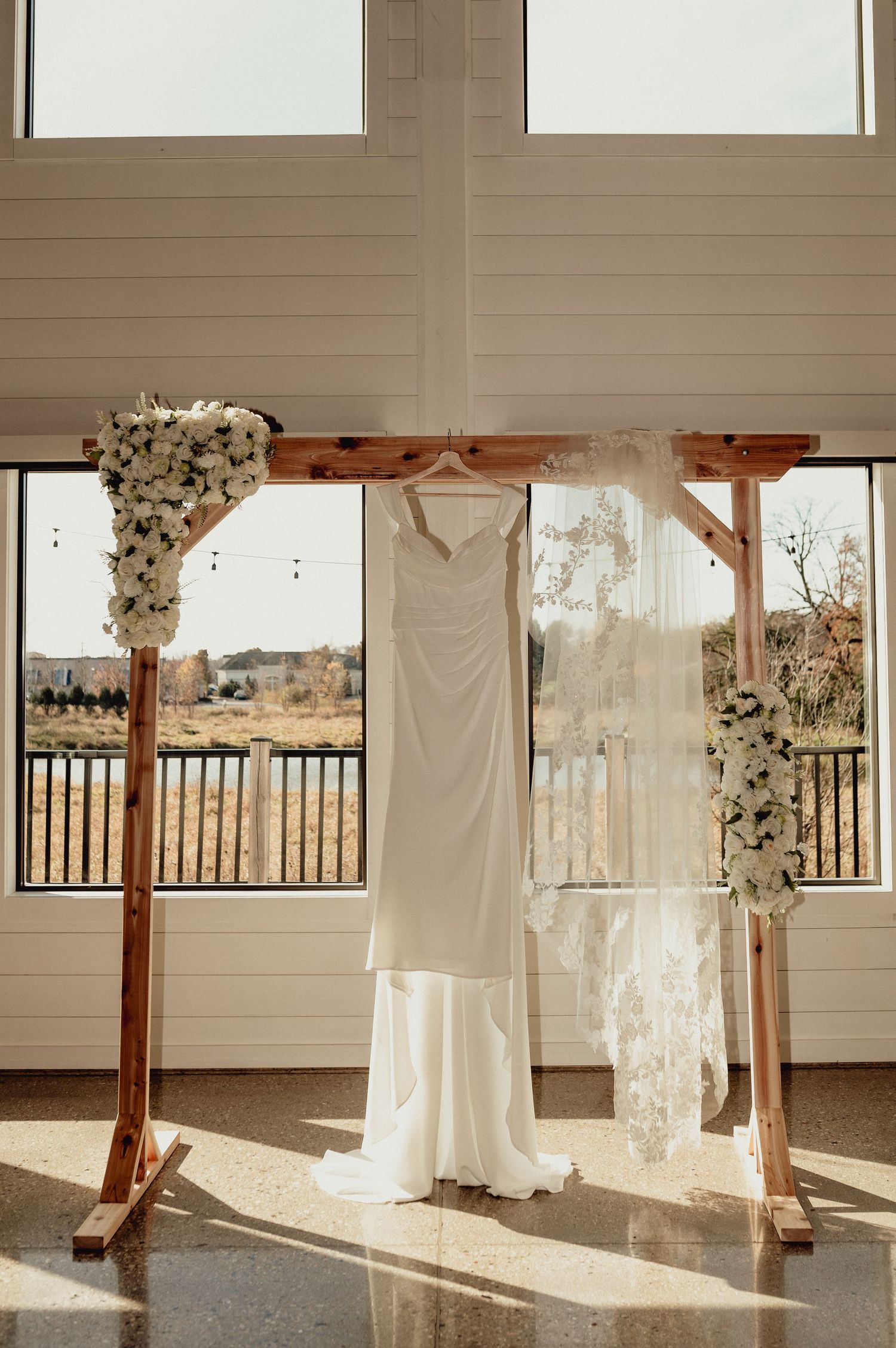 Wedding dresses hanging in a sunlit room with wooden beams and white decor create an ethereal bridal display.