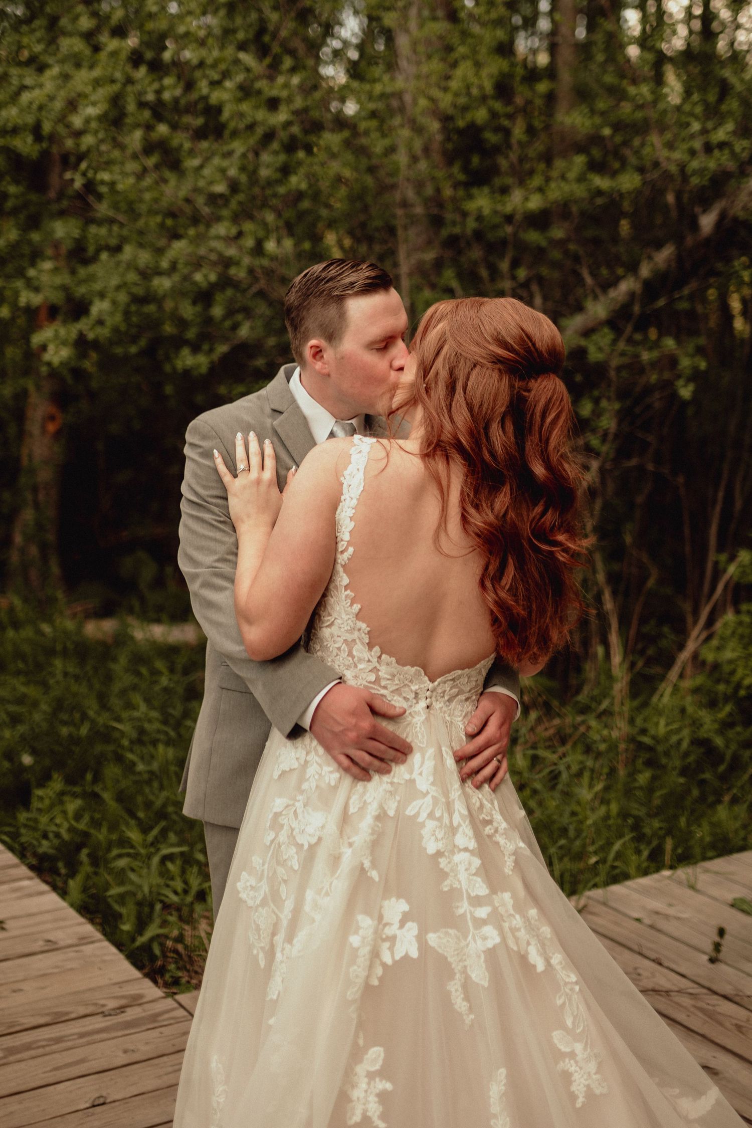 A romantic wedding couple embraces on a wooden deck surrounded by lush greenery during their outdoor photoshoot.
