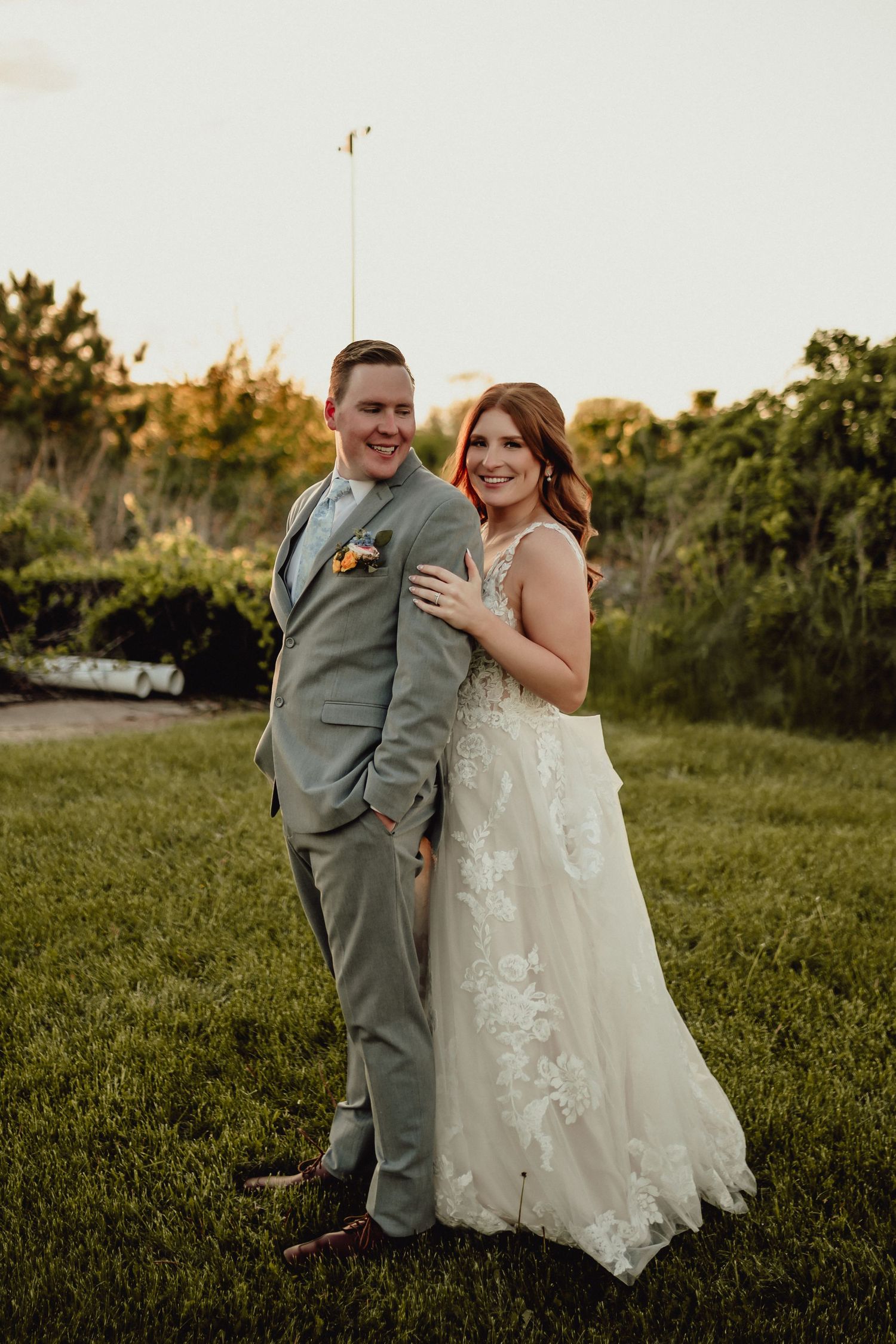 A couple shares a joyful moment in a grassy field during their wedding photoshoot at sunset.