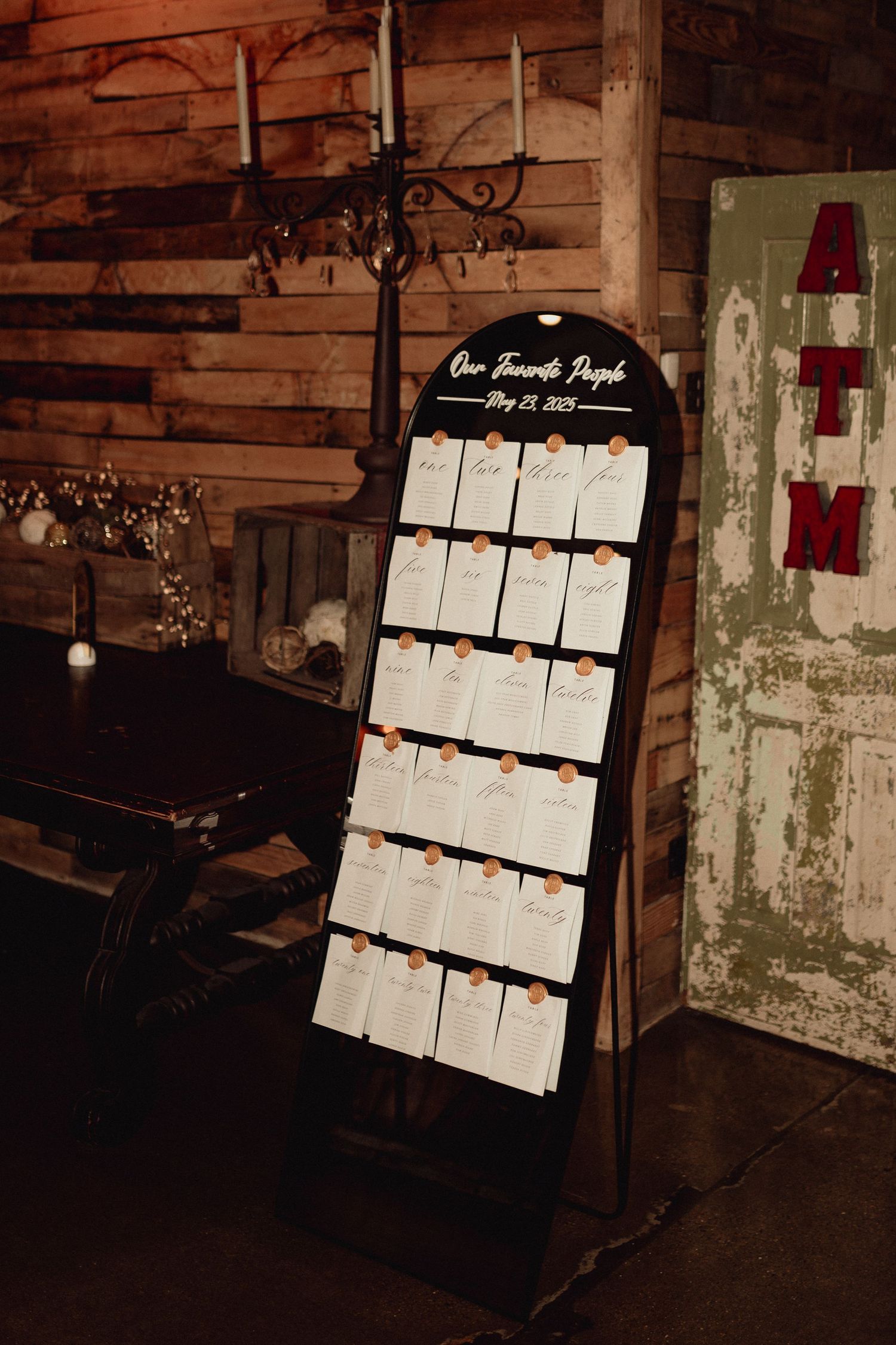 A rustic seating chart display board with white cards arranged against a weathered wooden wall at a wedding venue.