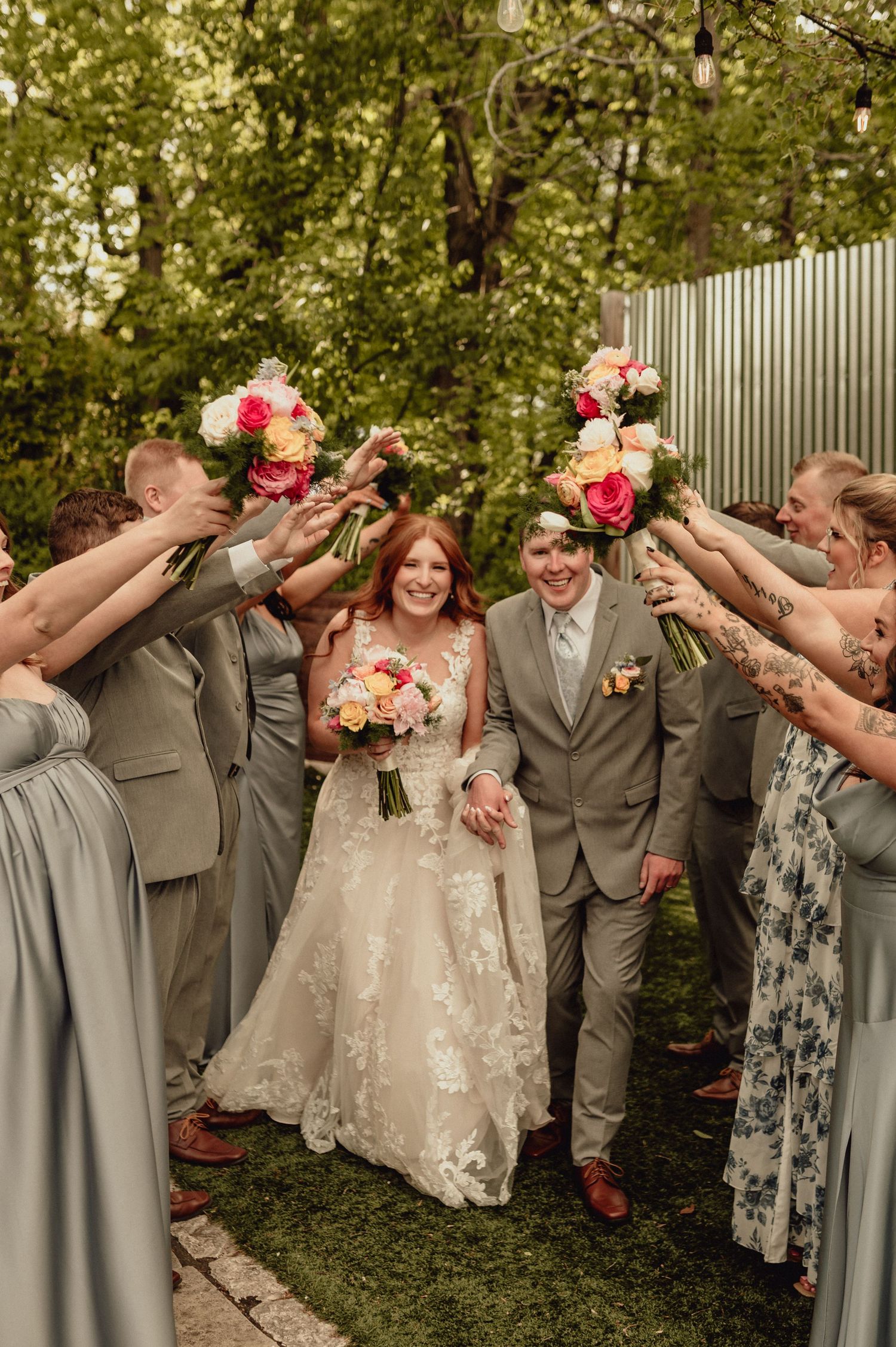 Wedding party in gray attire poses for a fun photo series showing a coordinated dabbing dance move in an outdoor garden setting.