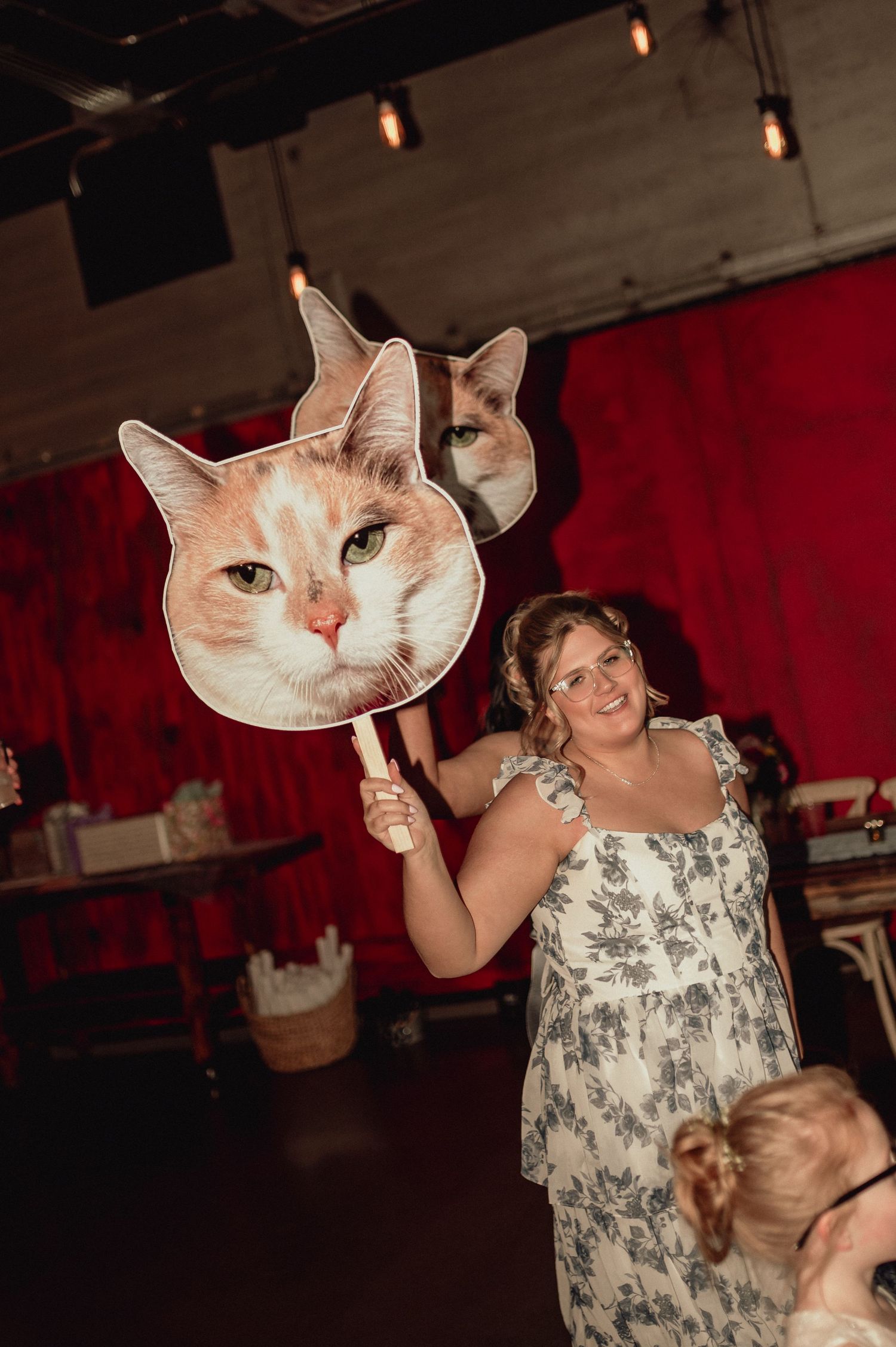 Party guests dancing and posing with oversized cat face cutouts against a red backdrop.
