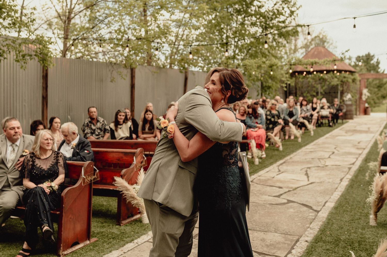Wedding guests mingle and celebrate outdoors during a festive garden reception at sunset.