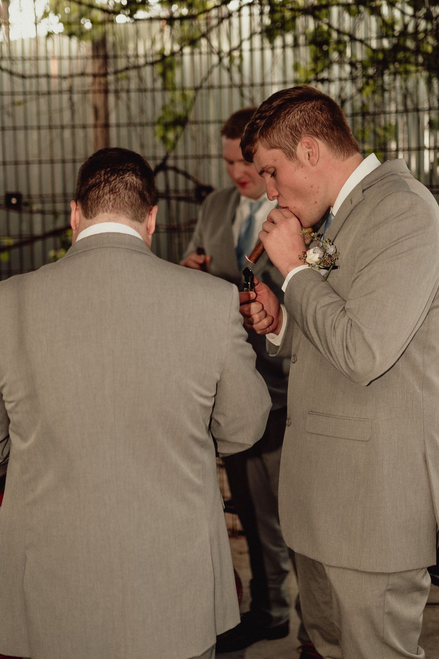 Groomsmen in light gray suits stand in a row during an outdoor wedding ceremony.