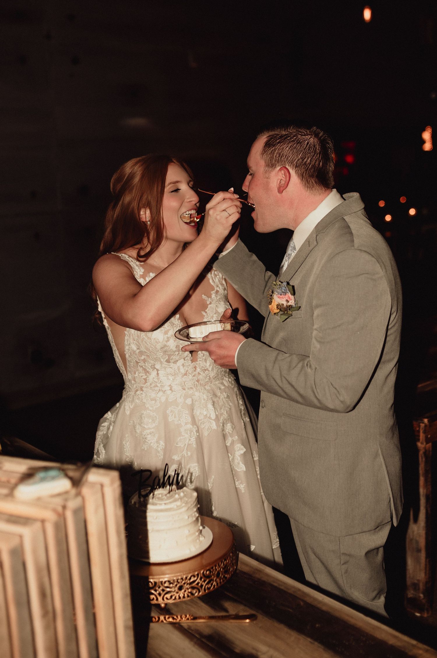 A couple shares their first bite of wedding cake together at their evening reception celebration.
