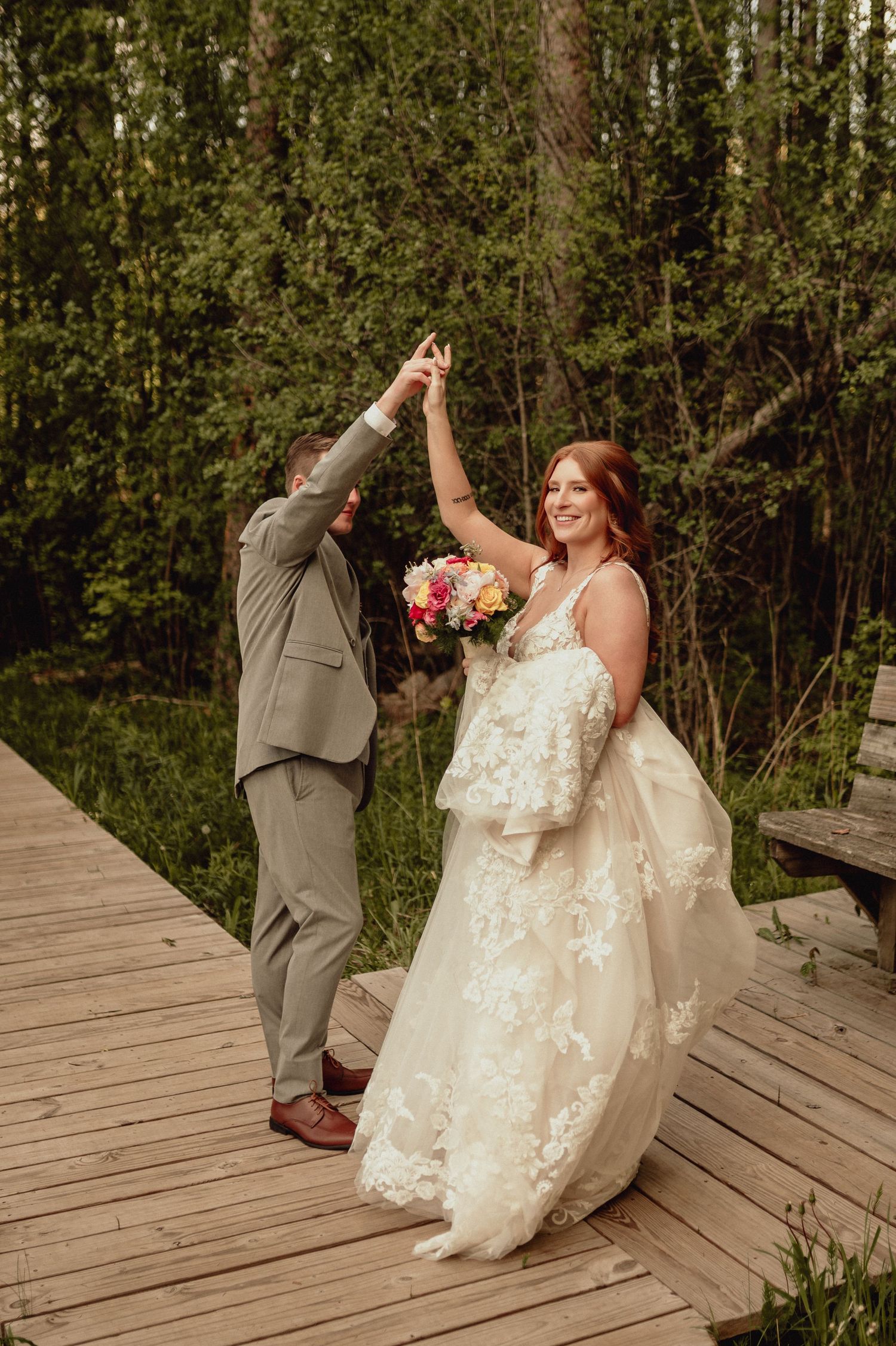 A couple dances together on a wooden deck surrounded by trees during a wedding celebration.