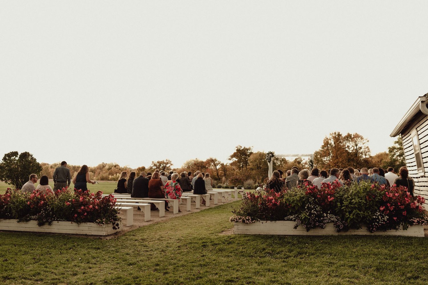 Panoramic view of wedding guests gathered outside a rustic venue during sunset.