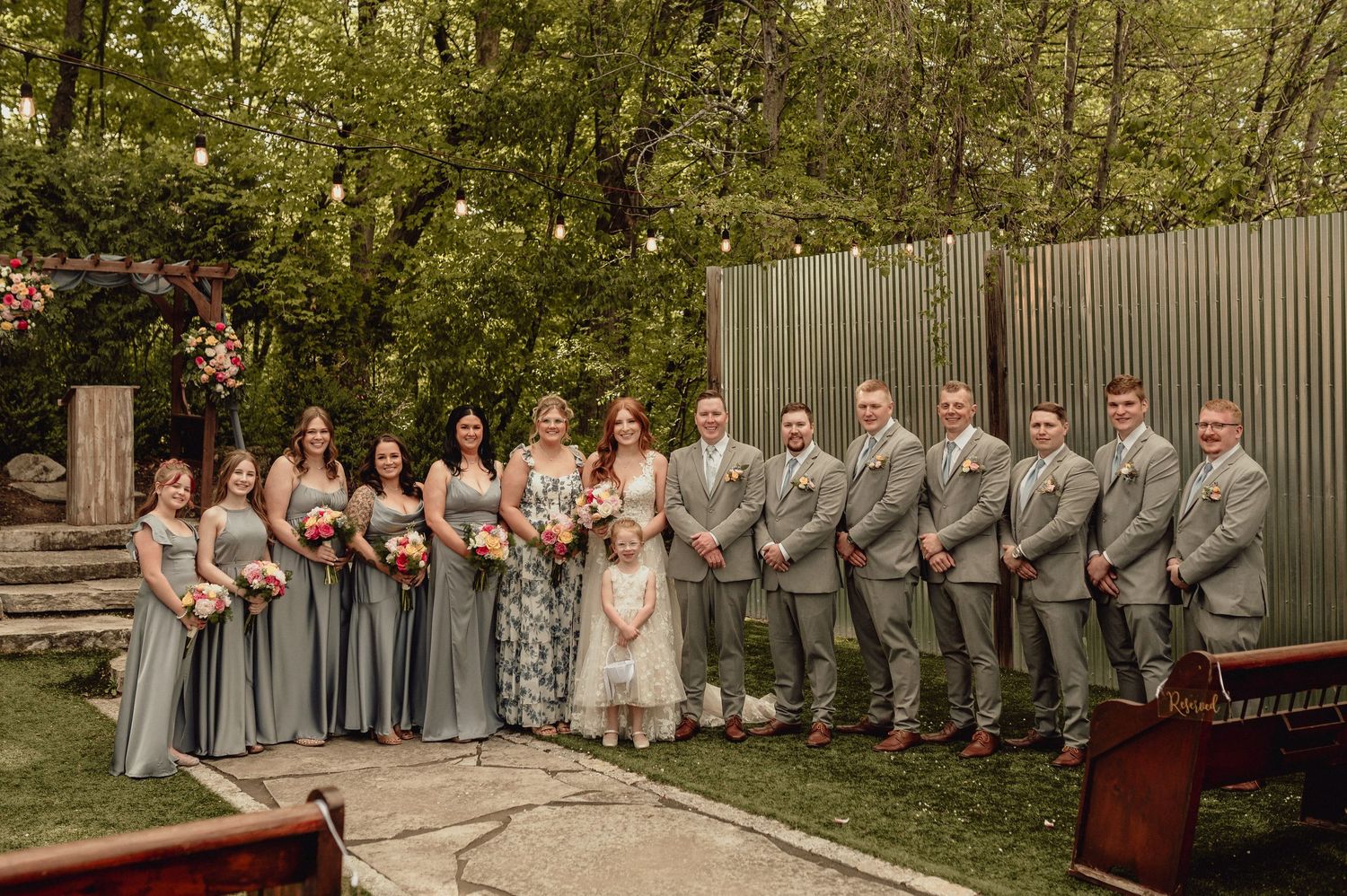 Wedding party stands in a row outdoors wearing gray and white formal attire during a spring celebration.