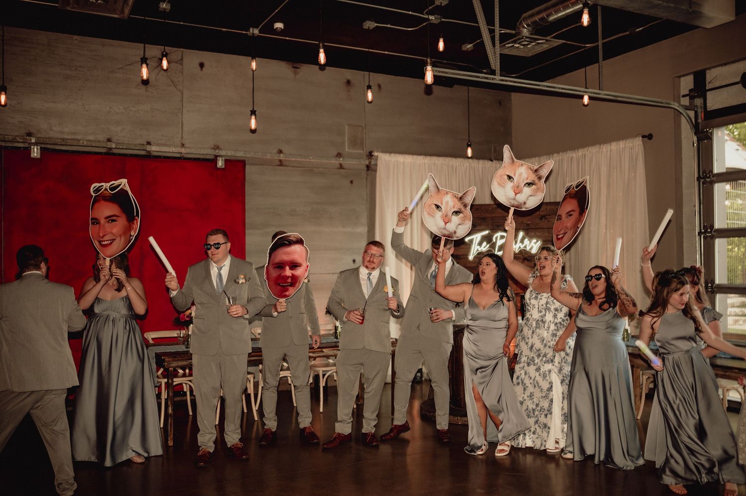 Wedding party in gray suits and bridesmaids in white dresses perform synchronized jumping pose for fun group photo.
