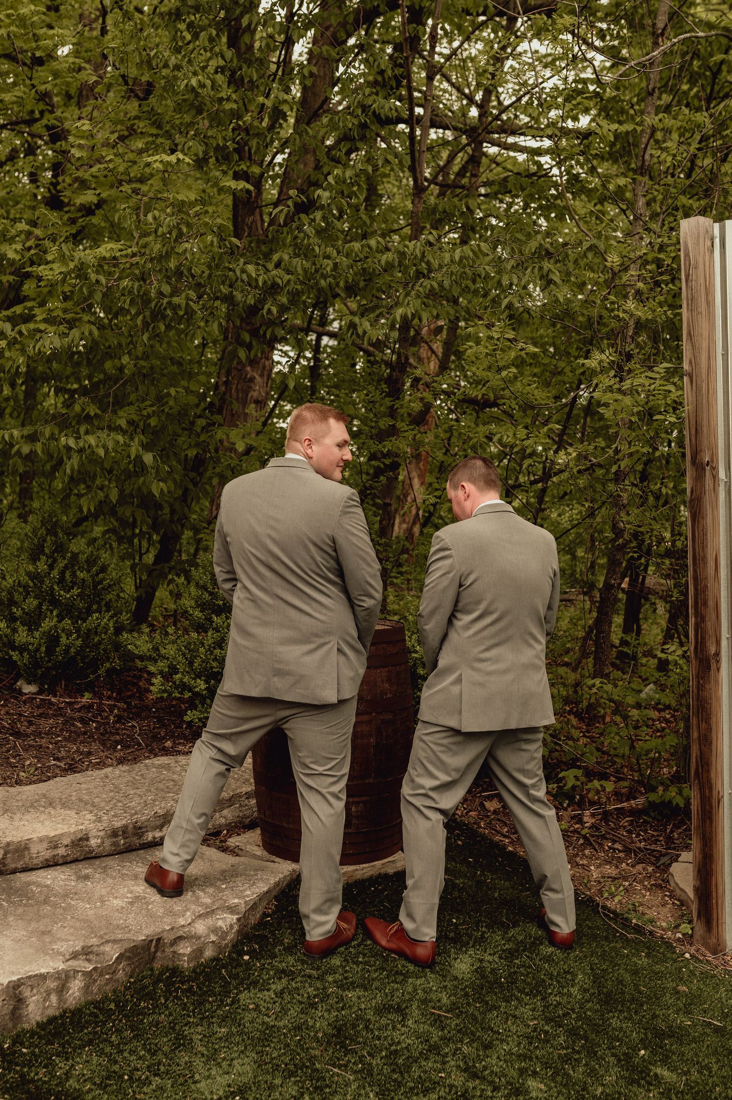 Two groomsmen in gray suits peek through bushes in a humorous sequence of wedding party photos in an outdoor setting.