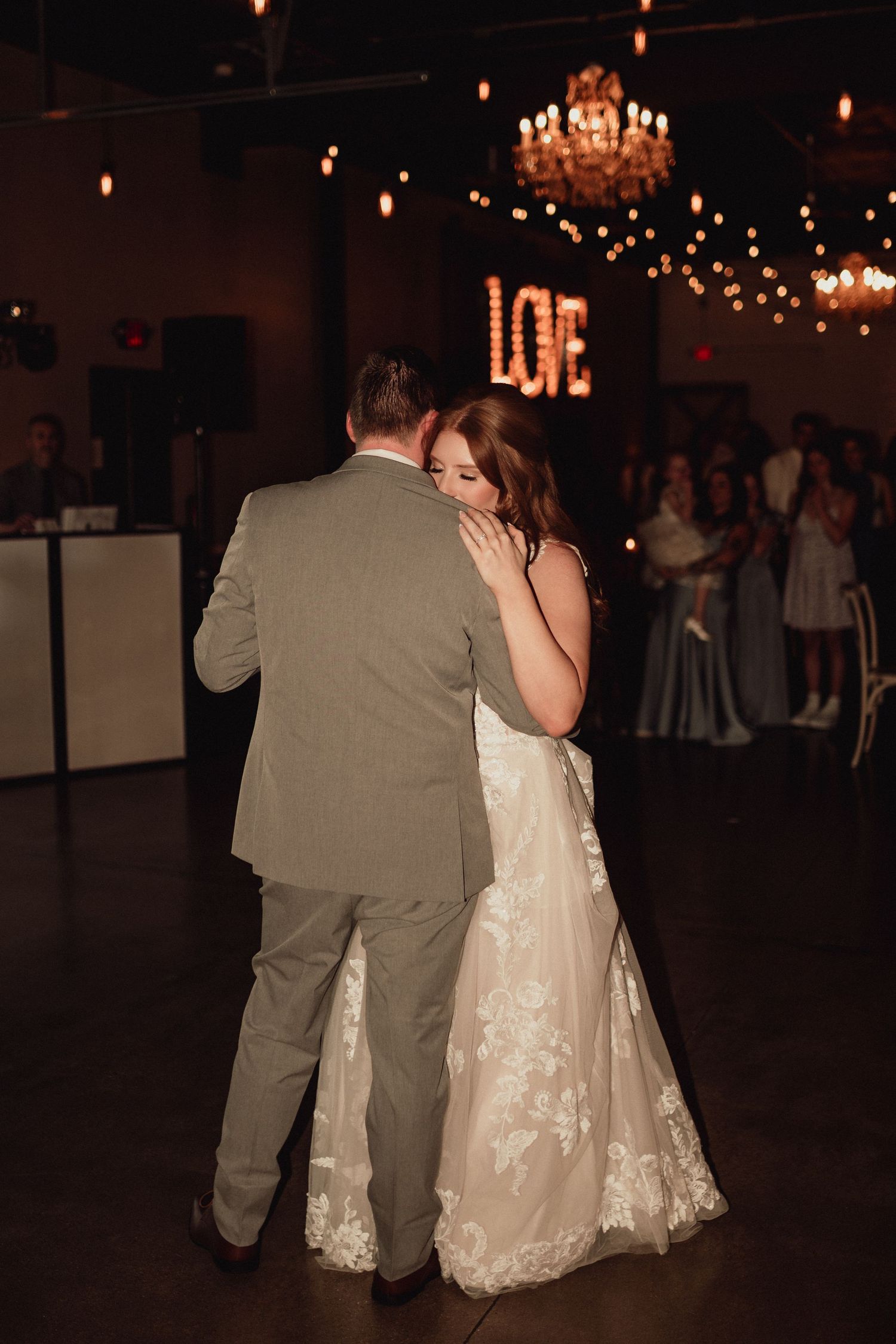 A bride and groom share their first dance at a wedding reception under elegant chandeliers.
