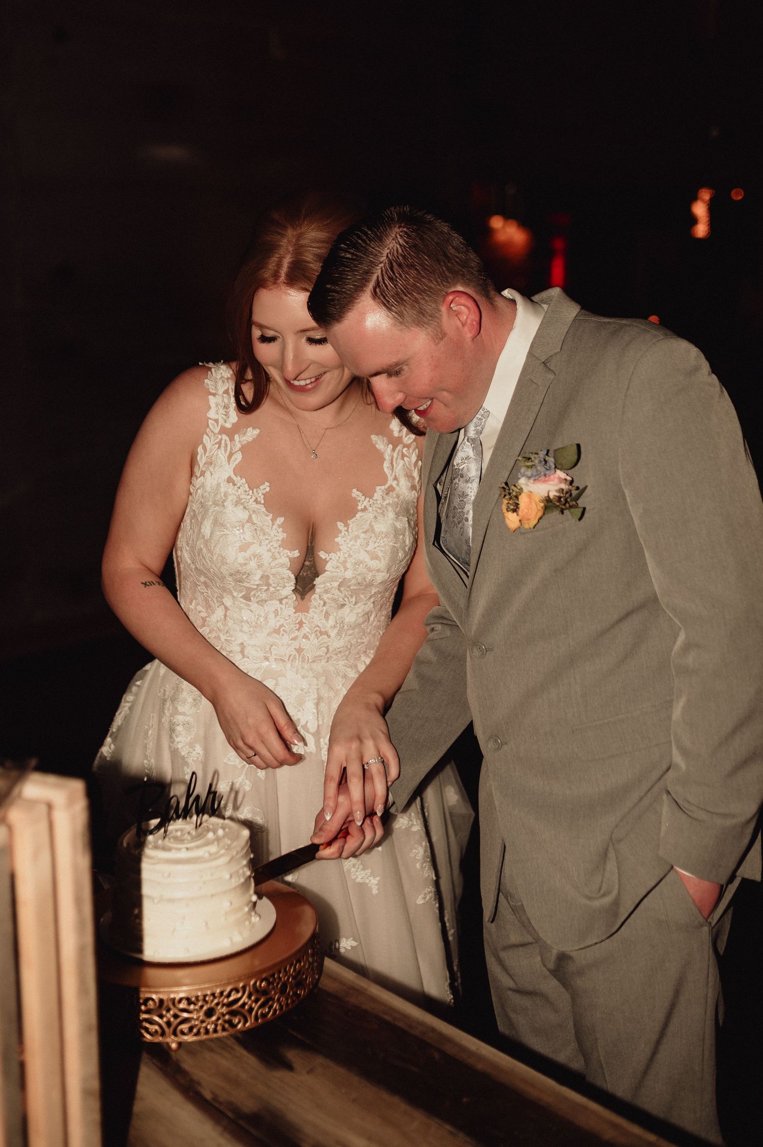 A couple in wedding attire cuts their wedding cake together in a dimly lit reception venue.