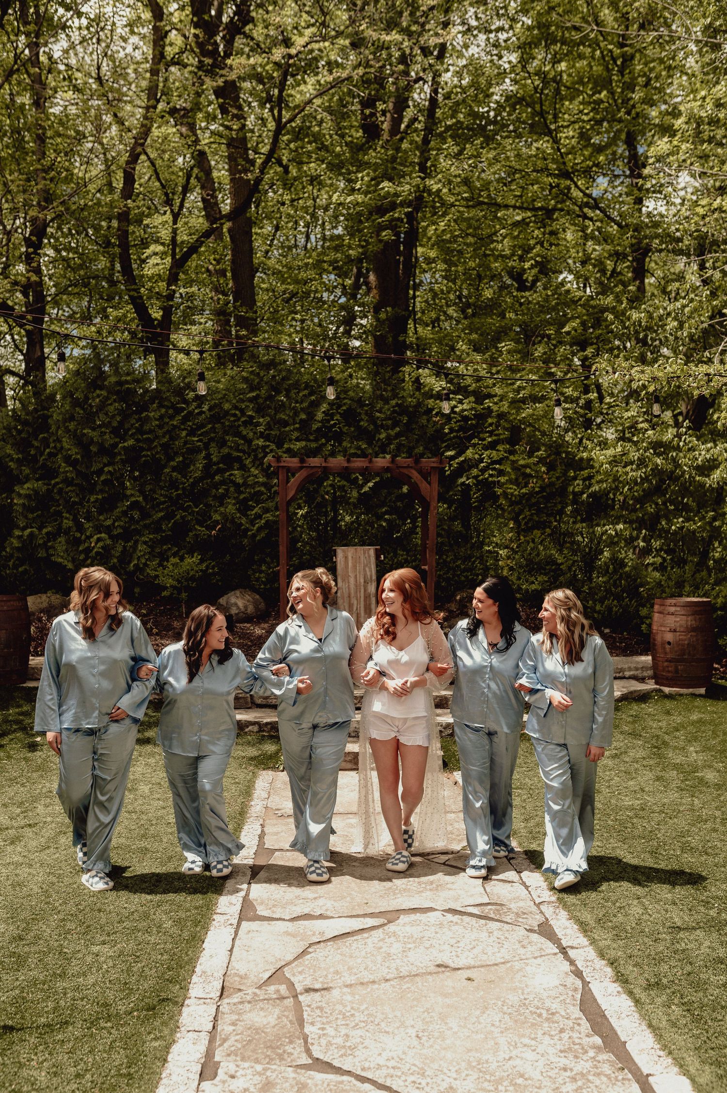 A group in matching gray outfits walking together and laughing in a backyard garden setting with trees and a wooden arch.