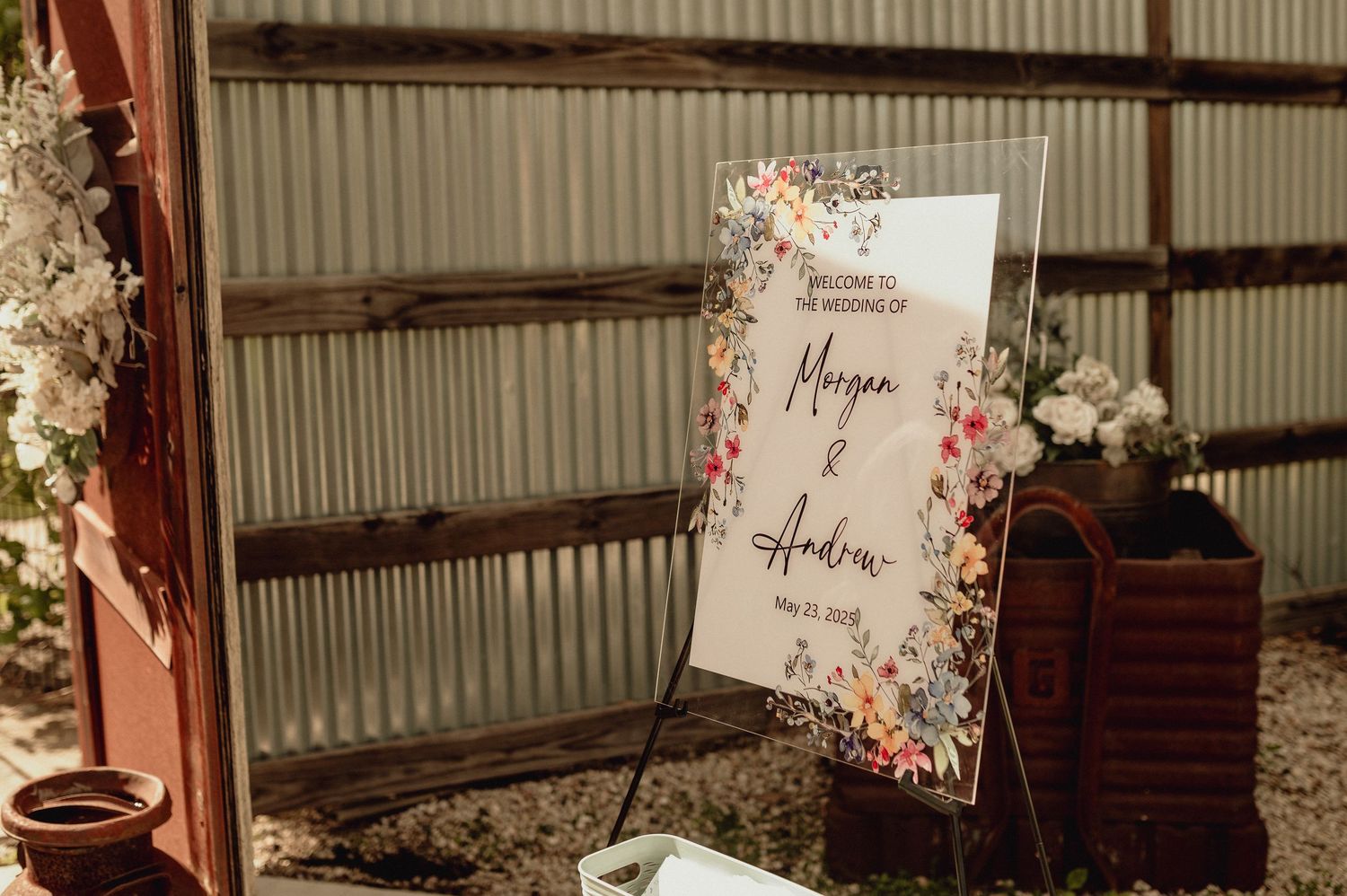 Rustic wedding venue interior with exposed metal beams and decorative floral signage hanging from ceiling.