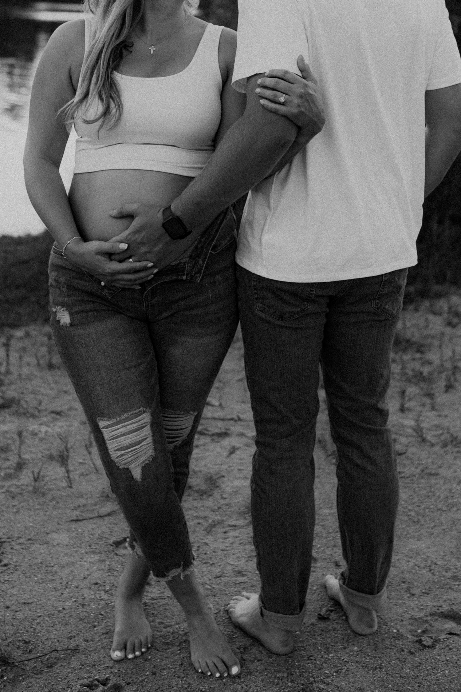 Black and white photo of barefoot couple standing together on outdoor ground.