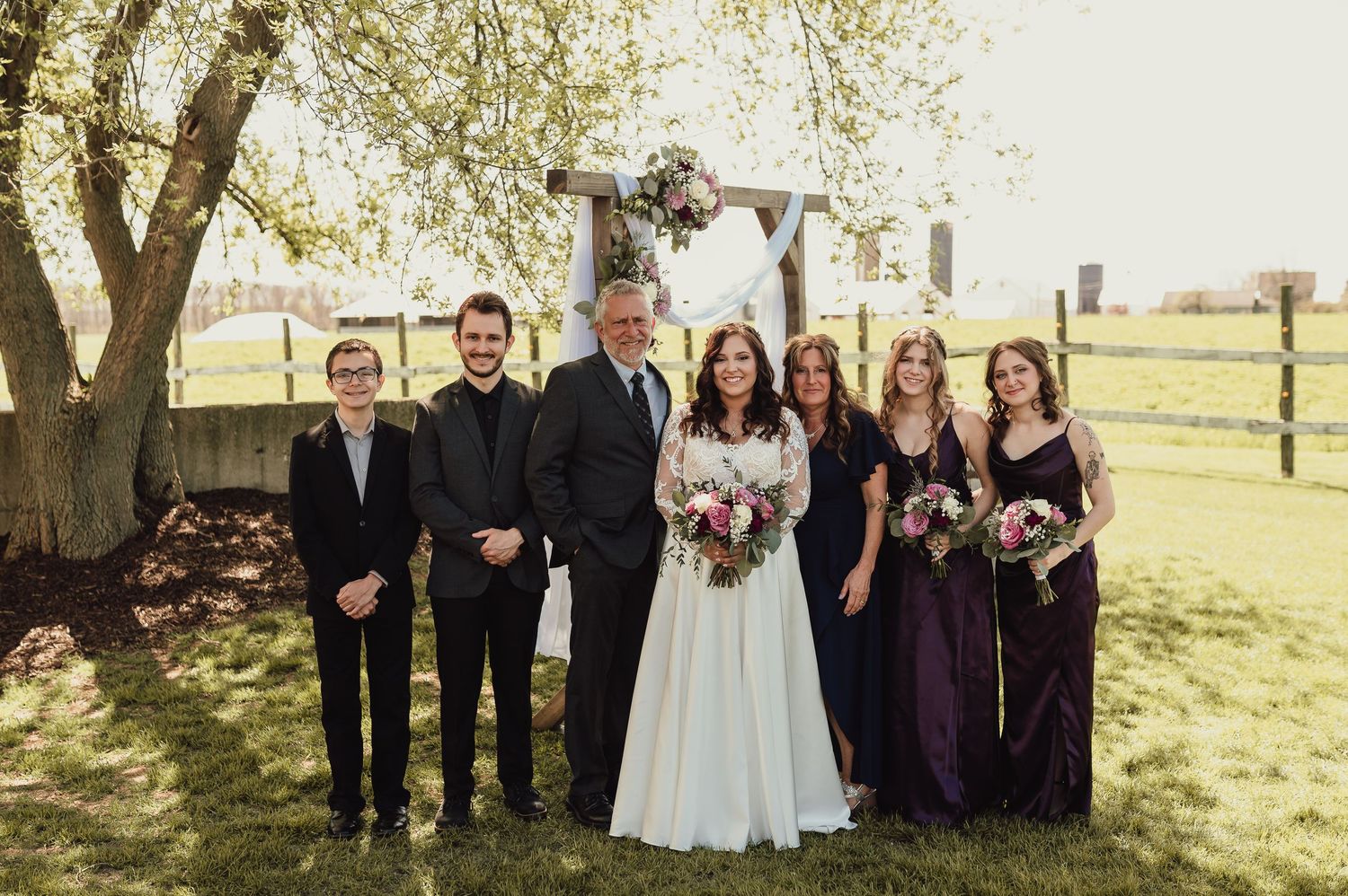 Wedding party lined up outdoors for group photos under trees.