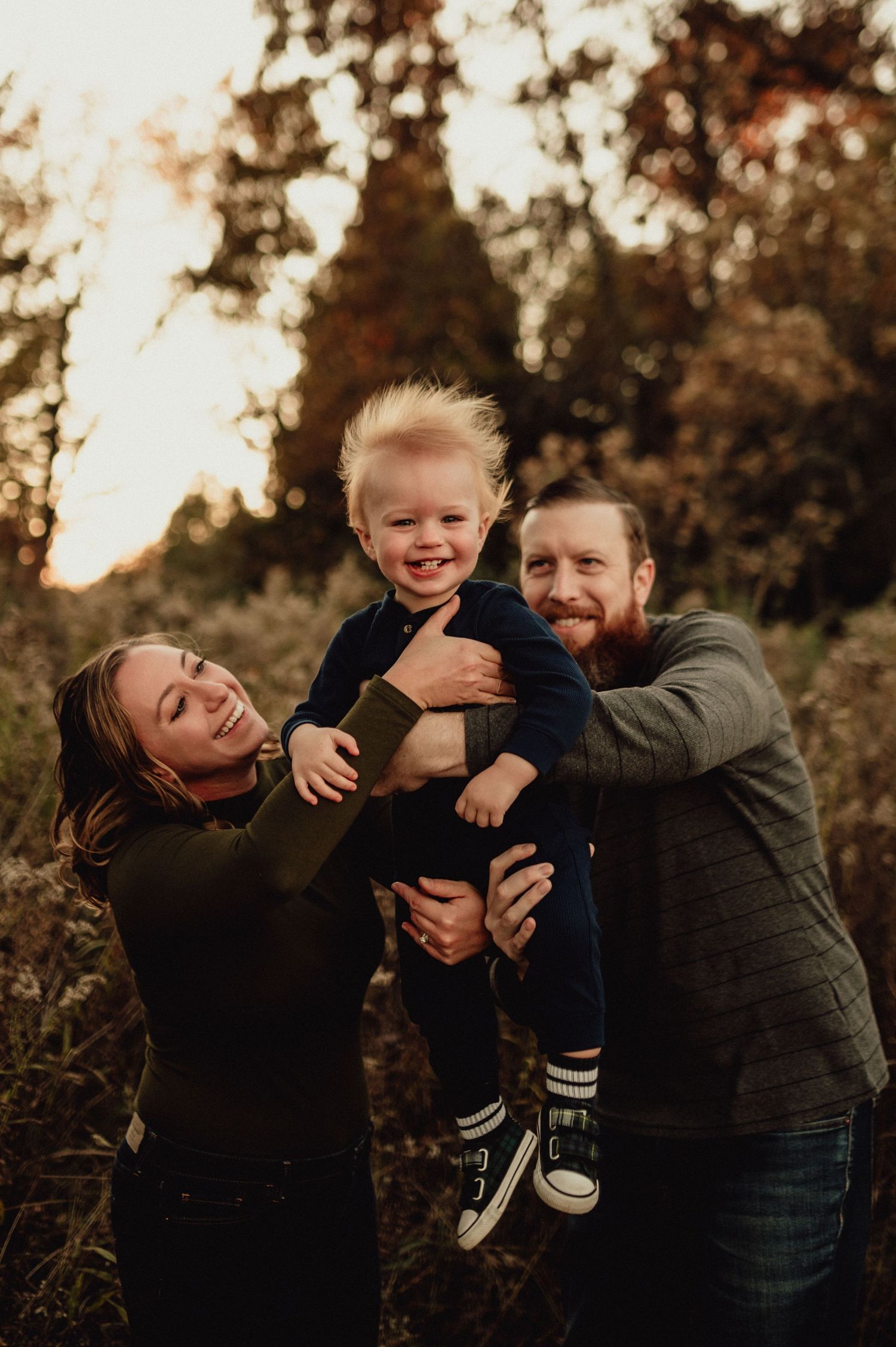 Family shares joyful moment lifting child together in autumn setting.