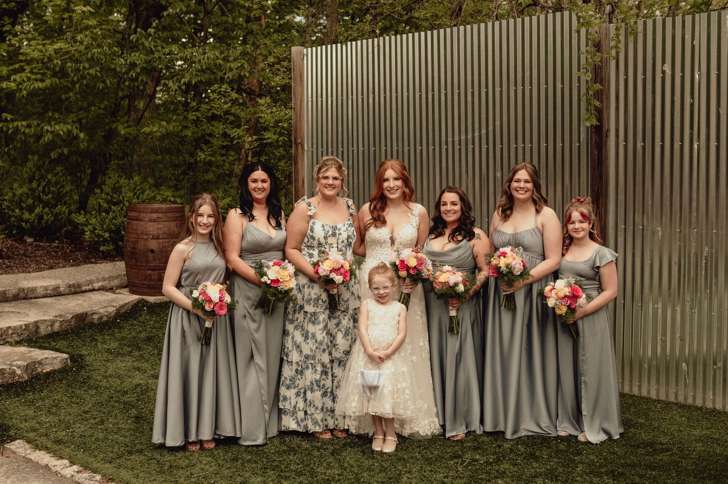 Bridesmaids in flowing gray dresses pose with colorful bouquets in an outdoor garden setting.