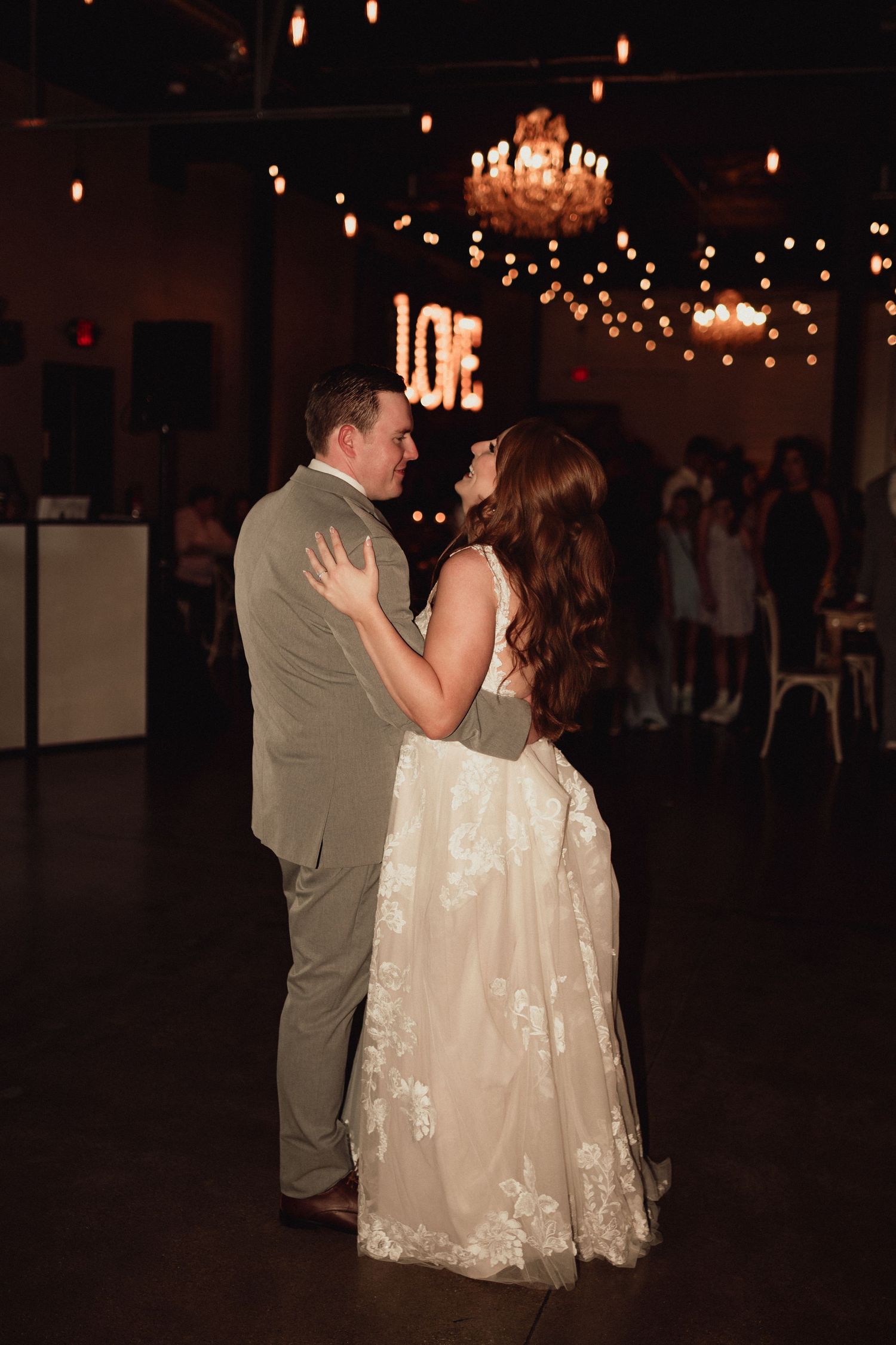 A couple shares their first dance at a wedding reception under warm lighting and romantic string lights.