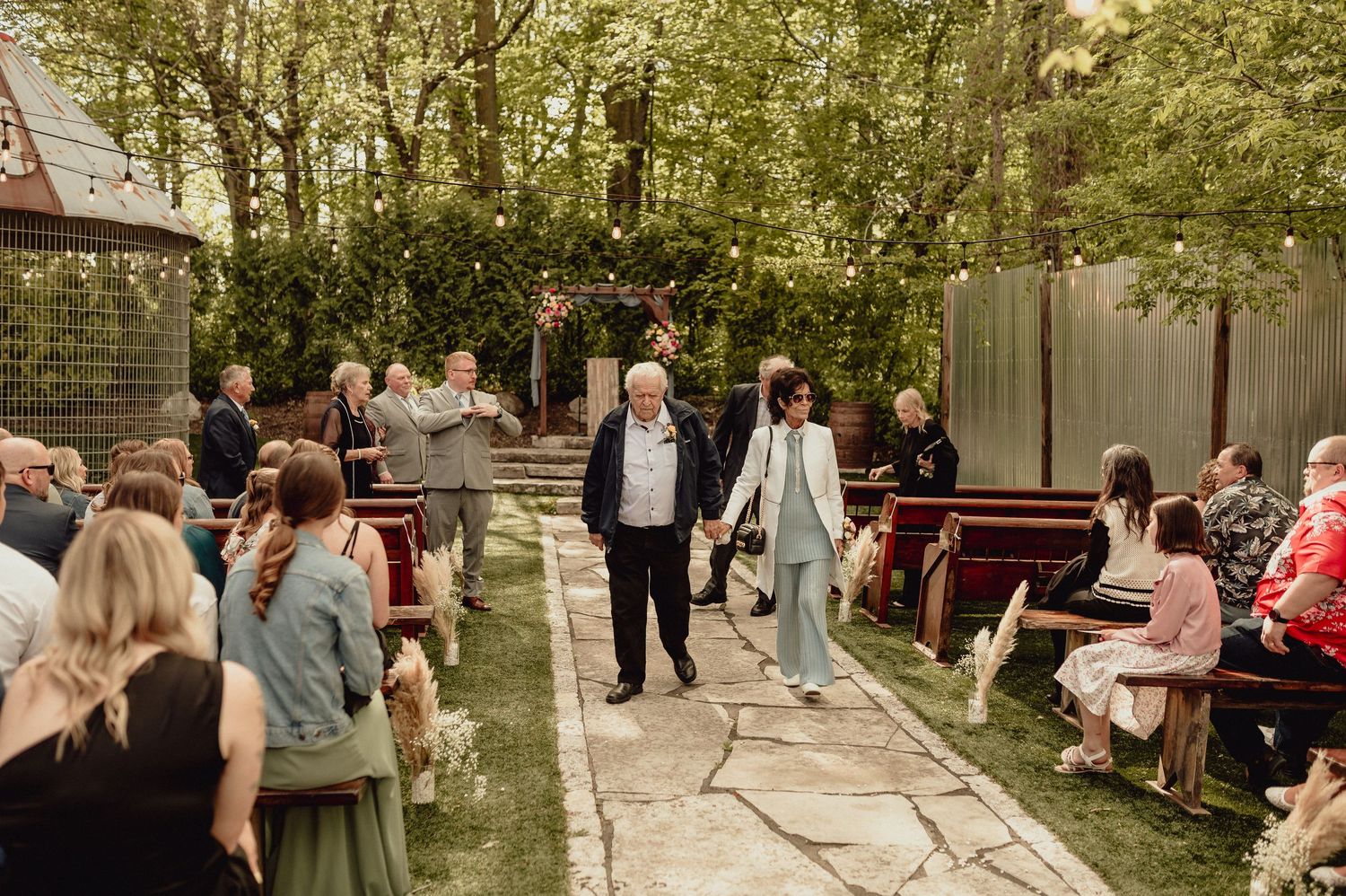 Wedding guests gather outdoors in a garden setting during a celebration event.