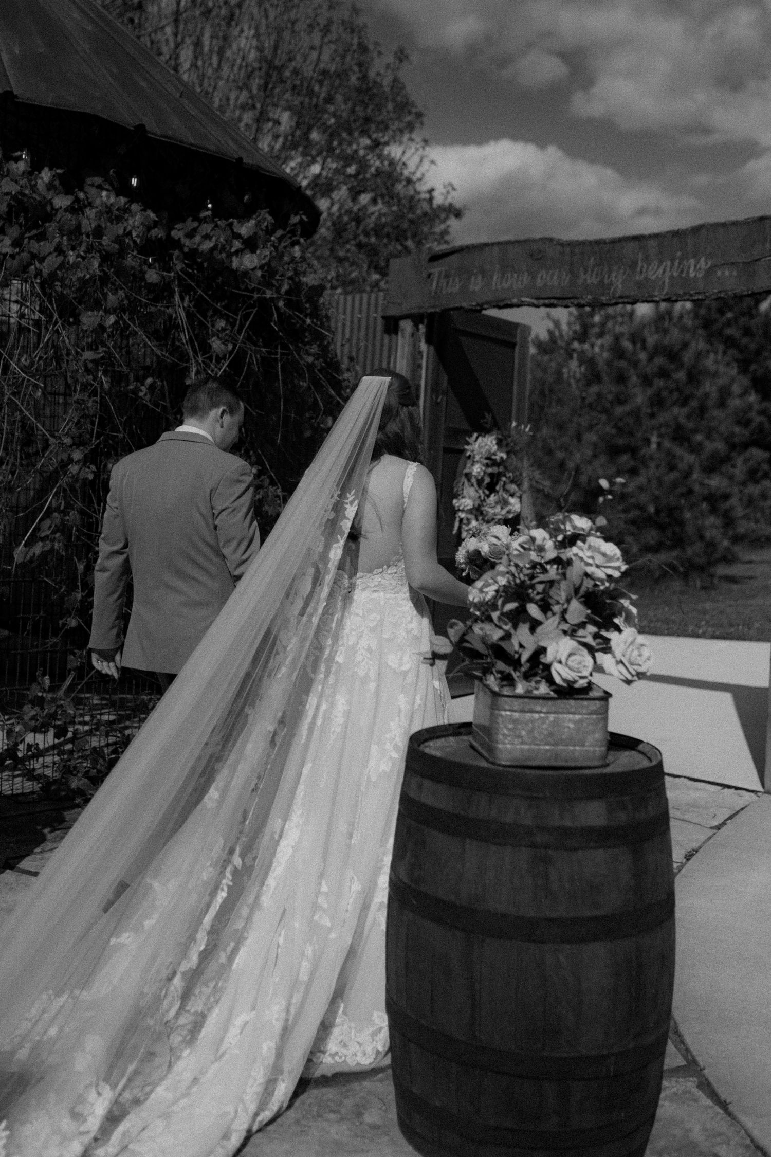 A series of black and white wedding photos showing a couple posing with wine barrels and floral arrangements outdoors.