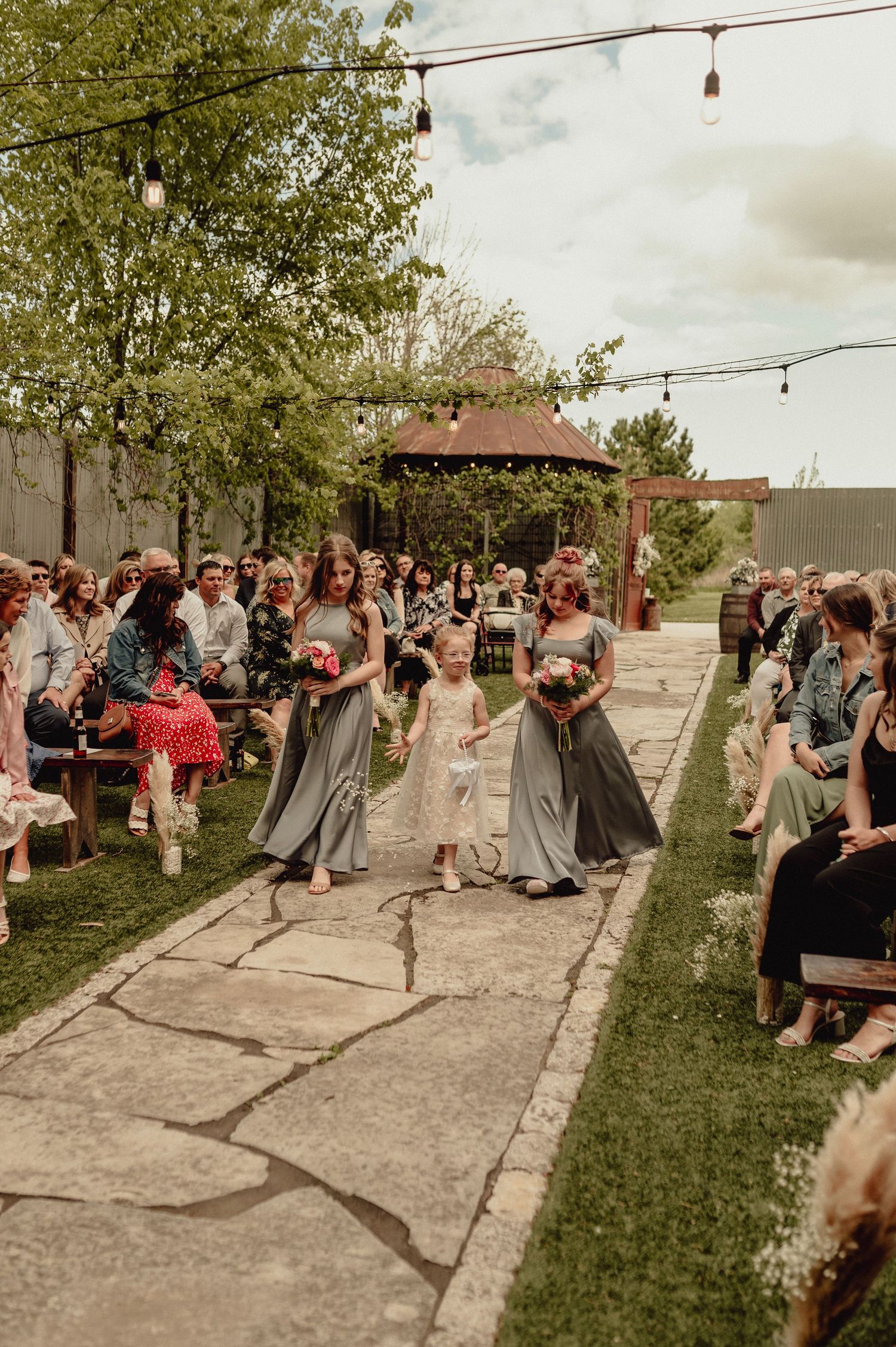 Wedding guests dance together on a concrete patio under string lights at an outdoor reception venue.