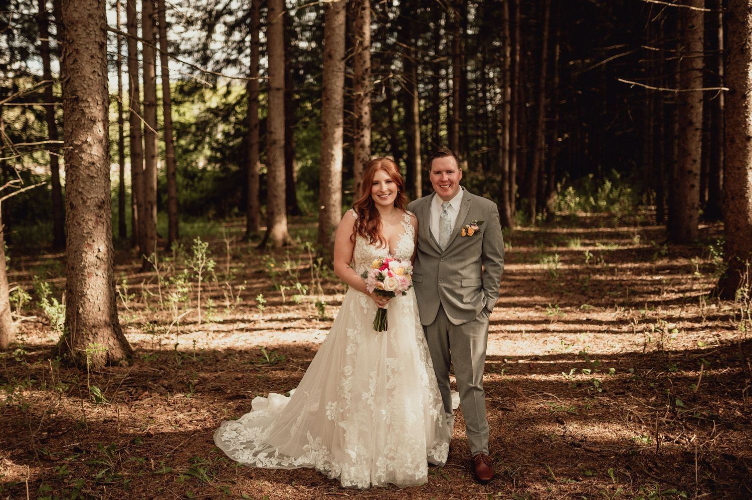 A couple in wedding attire poses in a sunlit forest setting during their wedding photo session.